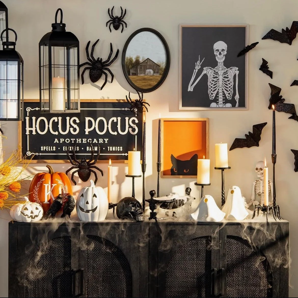 Halloween and spooky-themed decorations on a black sideboard, including pumpkins, skulls, ghosts, candles, spiders, bats, a skeleton, and a sign reading 'Hocus Pocus Apothecary' with cobwebs.