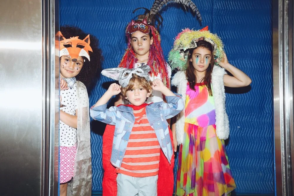 Four children dressed in colorful costumes posing for a photo in an elevator.
