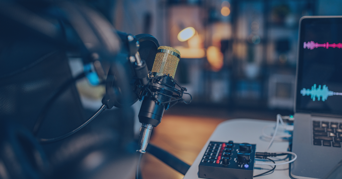 A professional recording setup with a gold microphone on a stand, a laptop displaying audio waveforms, and an audio mixer on a table.