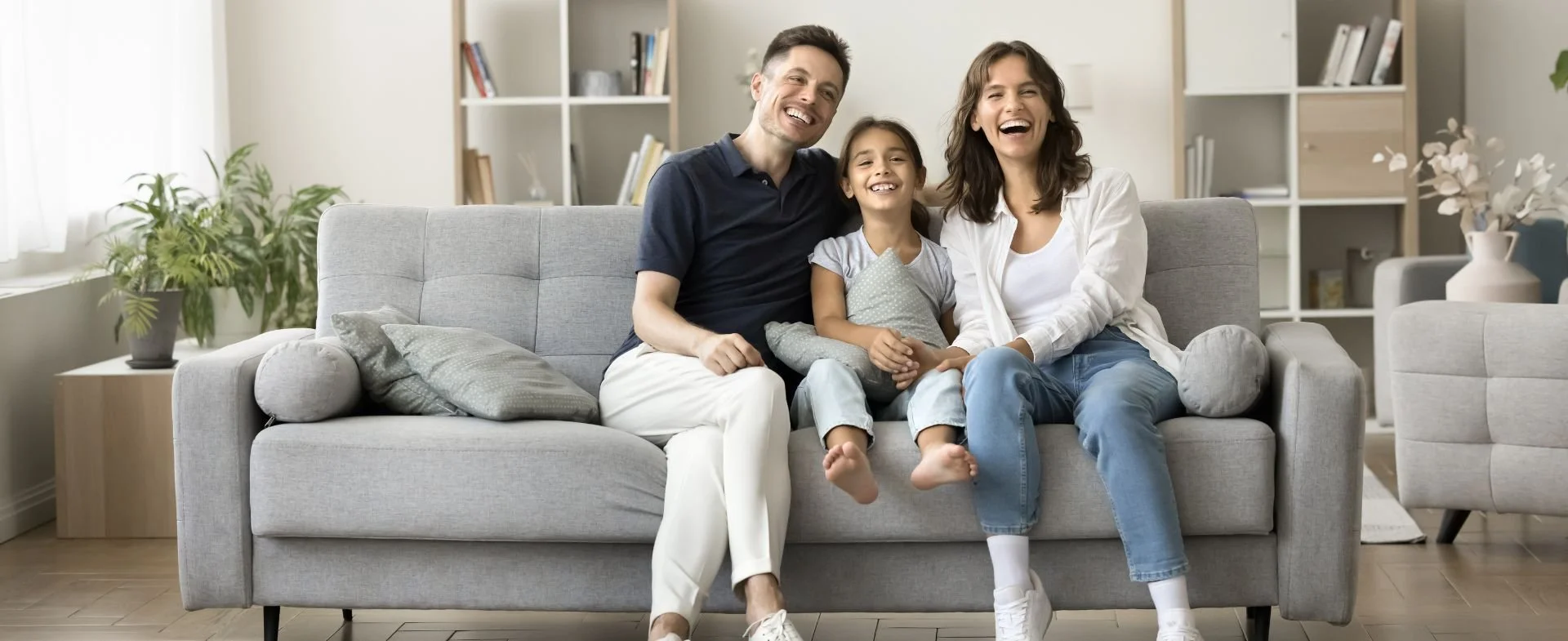 A family of four sitting on a gray sofa in a living room, smiling and enjoying each other's company.