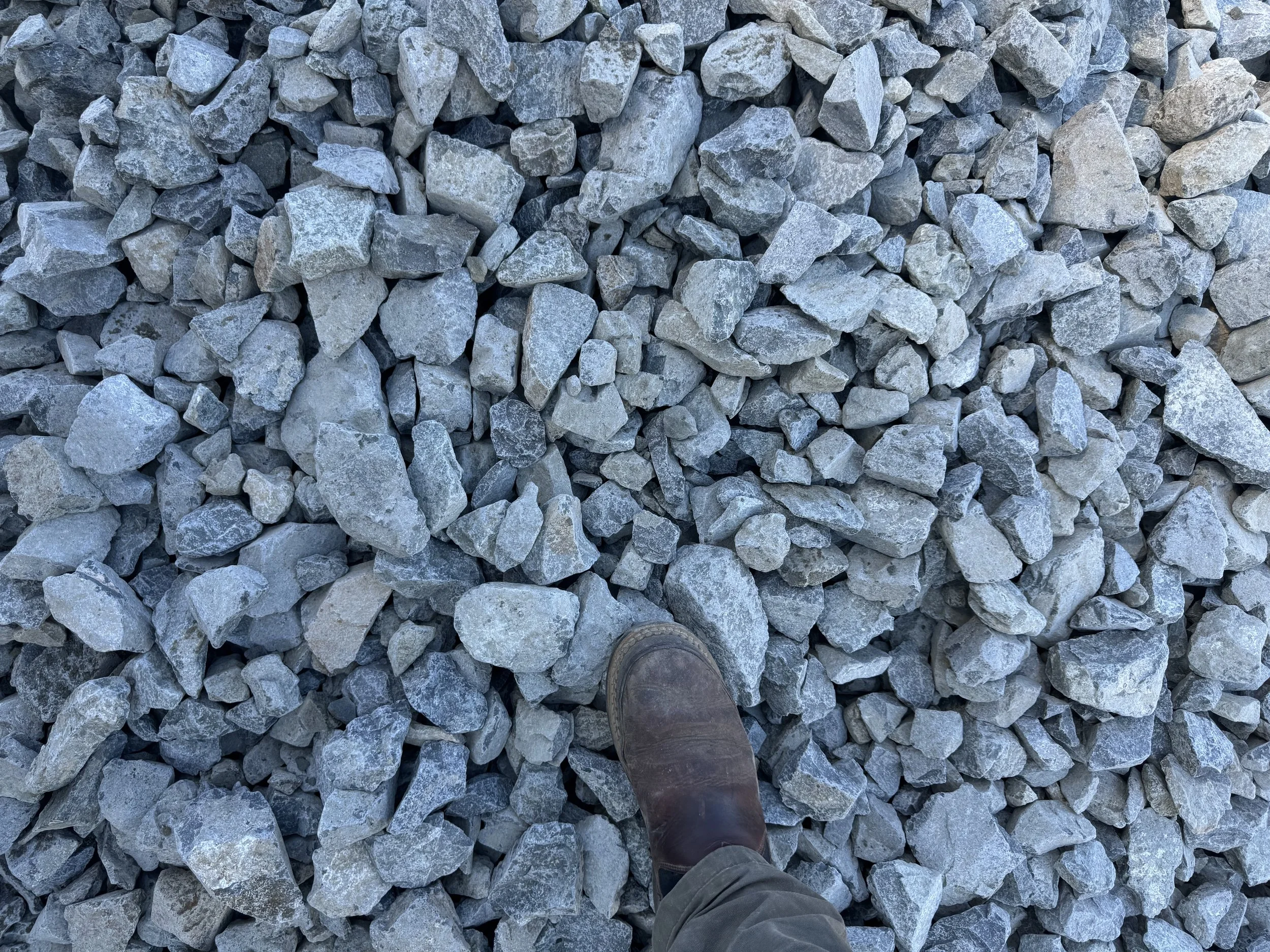 A person wearing a brown boot standing on a bed of gray rocks.