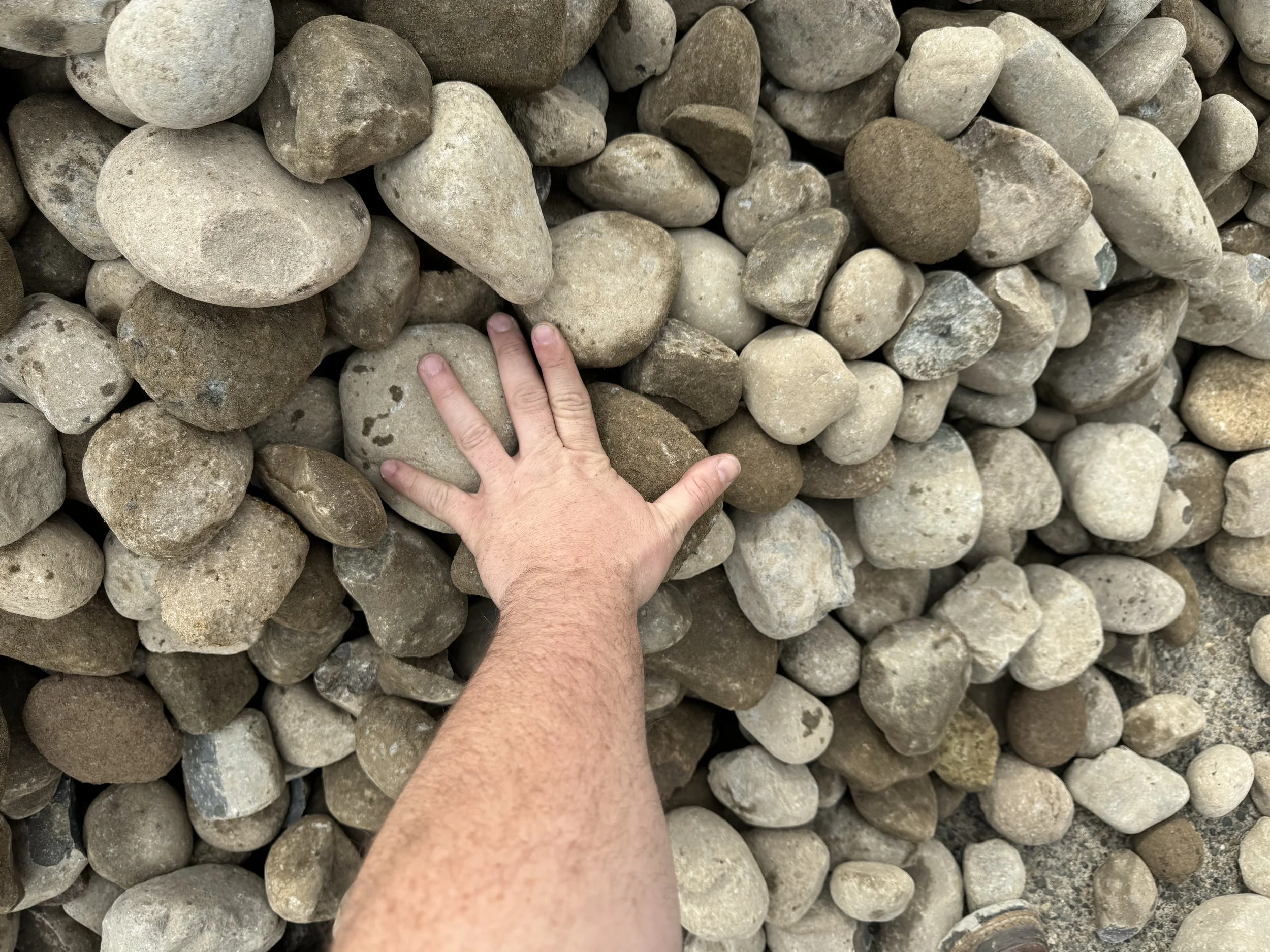 A hand placing on a pile of large, smooth, rounded rocks of various shades of gray and brown.