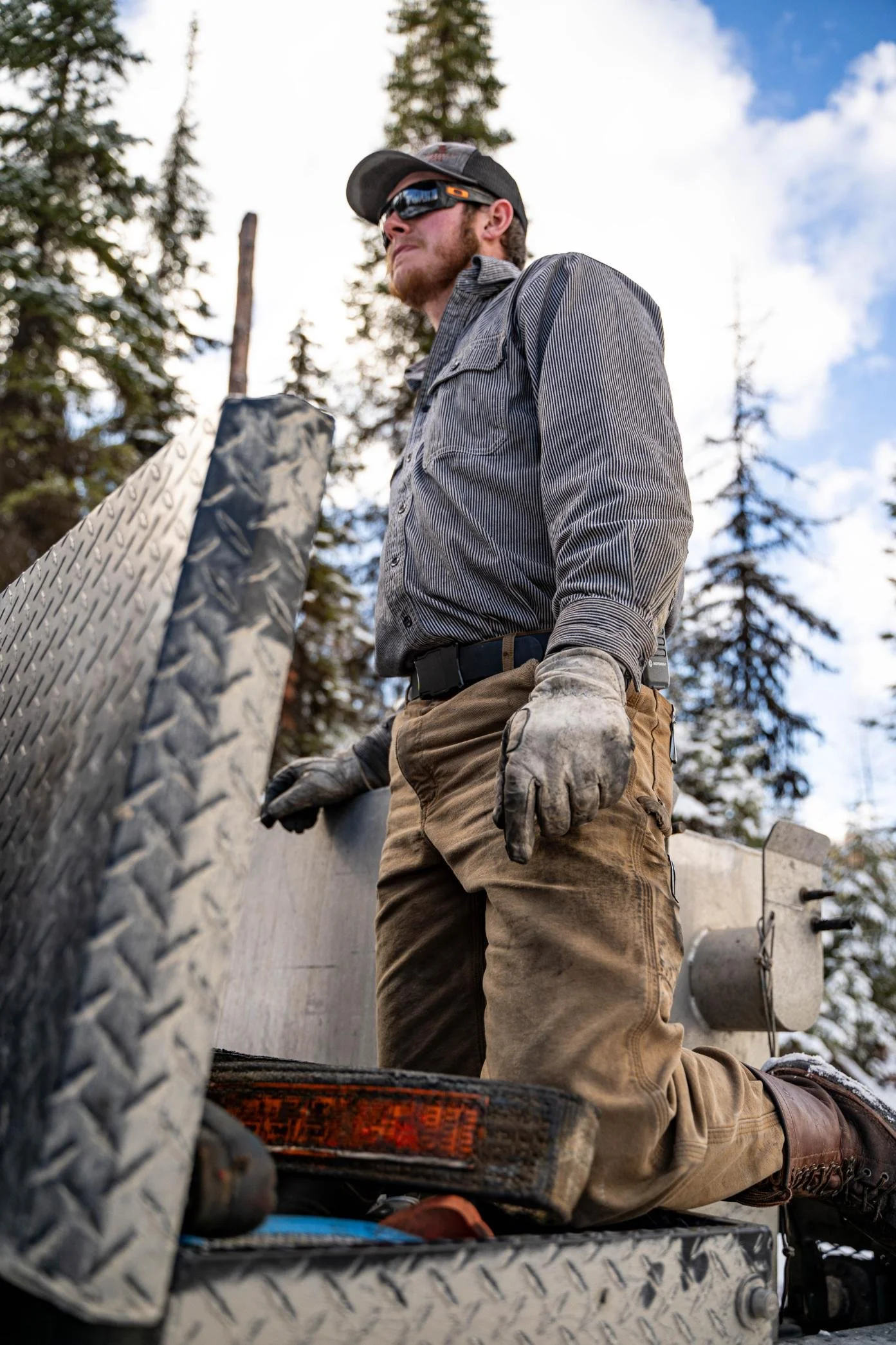 Side view from below of a man leaning against an open toolbox in the back of a truck, looking straight ahead over the camera, captured during the Apogee Belt field test photoshoot in Northwest Montana
