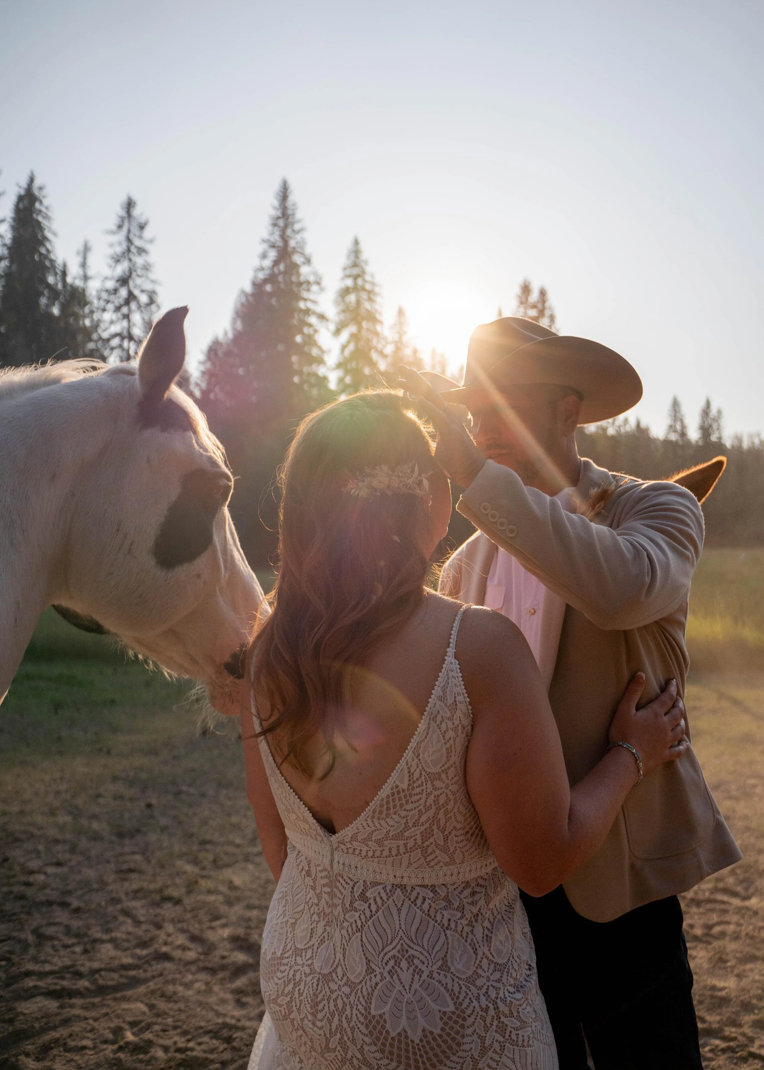 Groom gently brushing his bride’s hair from her face while holding her close, standing next to a pinto horse, captured during a wedding photoshoot in Flathead Valley, Montana.