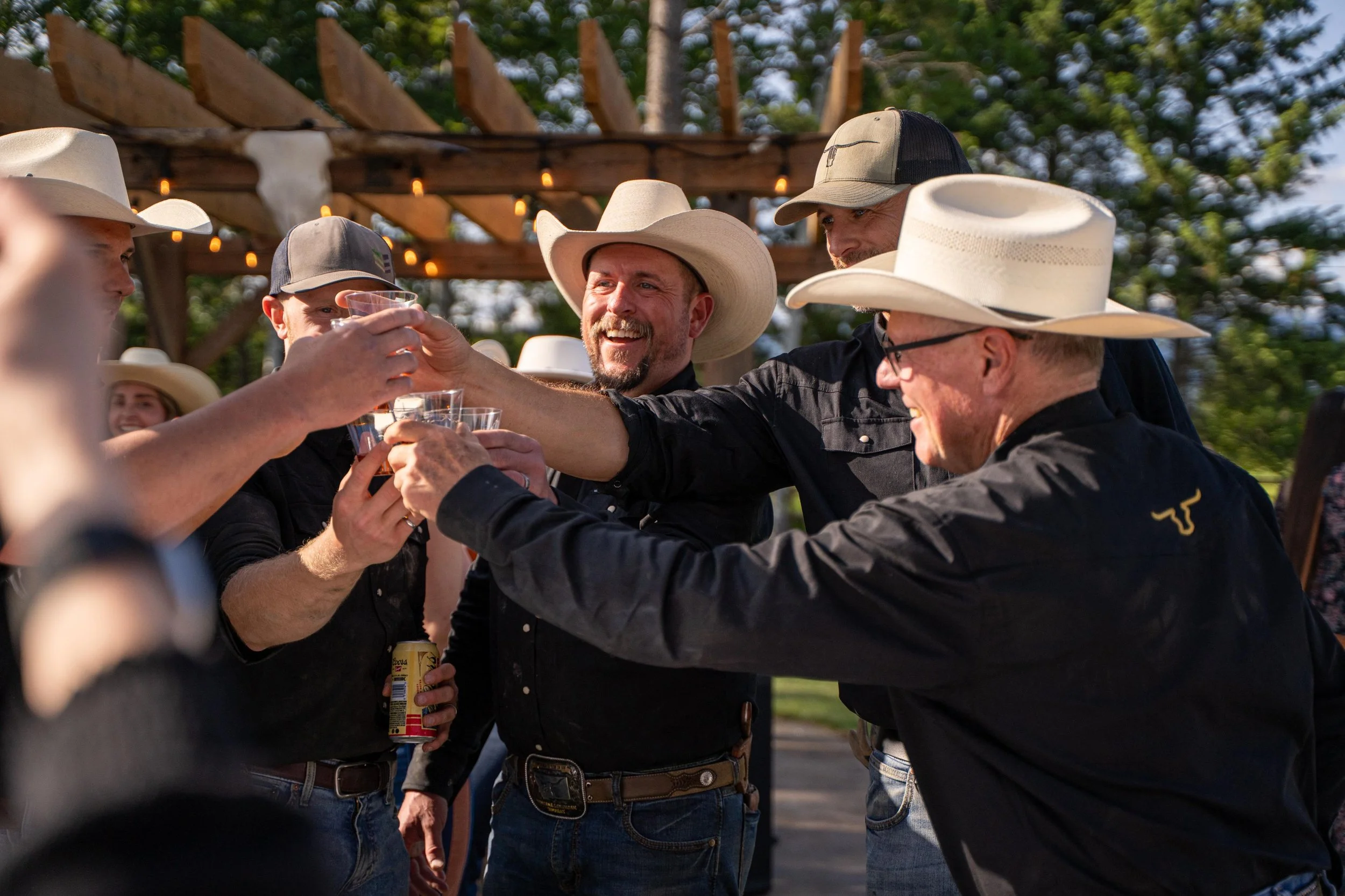 Group of cowboys clinking their glasses together in celebration after a day of hard work at Montana Longhorn Ranch, captured during a ranch lifestyle photoshoot.