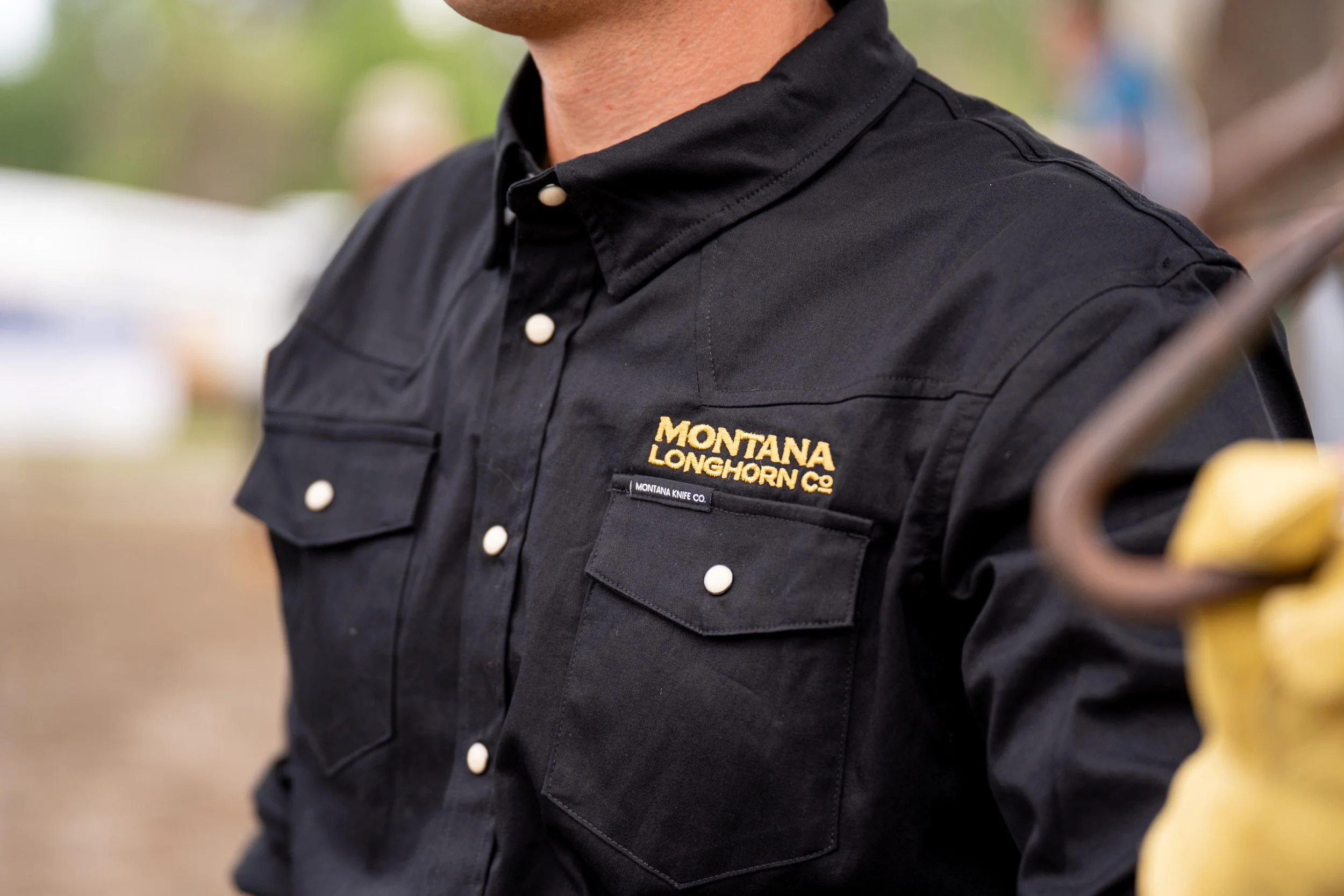 Close-up of a man wearing a black western shirt embroidered with ‘Montana Longhorn Co.’ over the breast pocket, captured during a ranch photoshoot