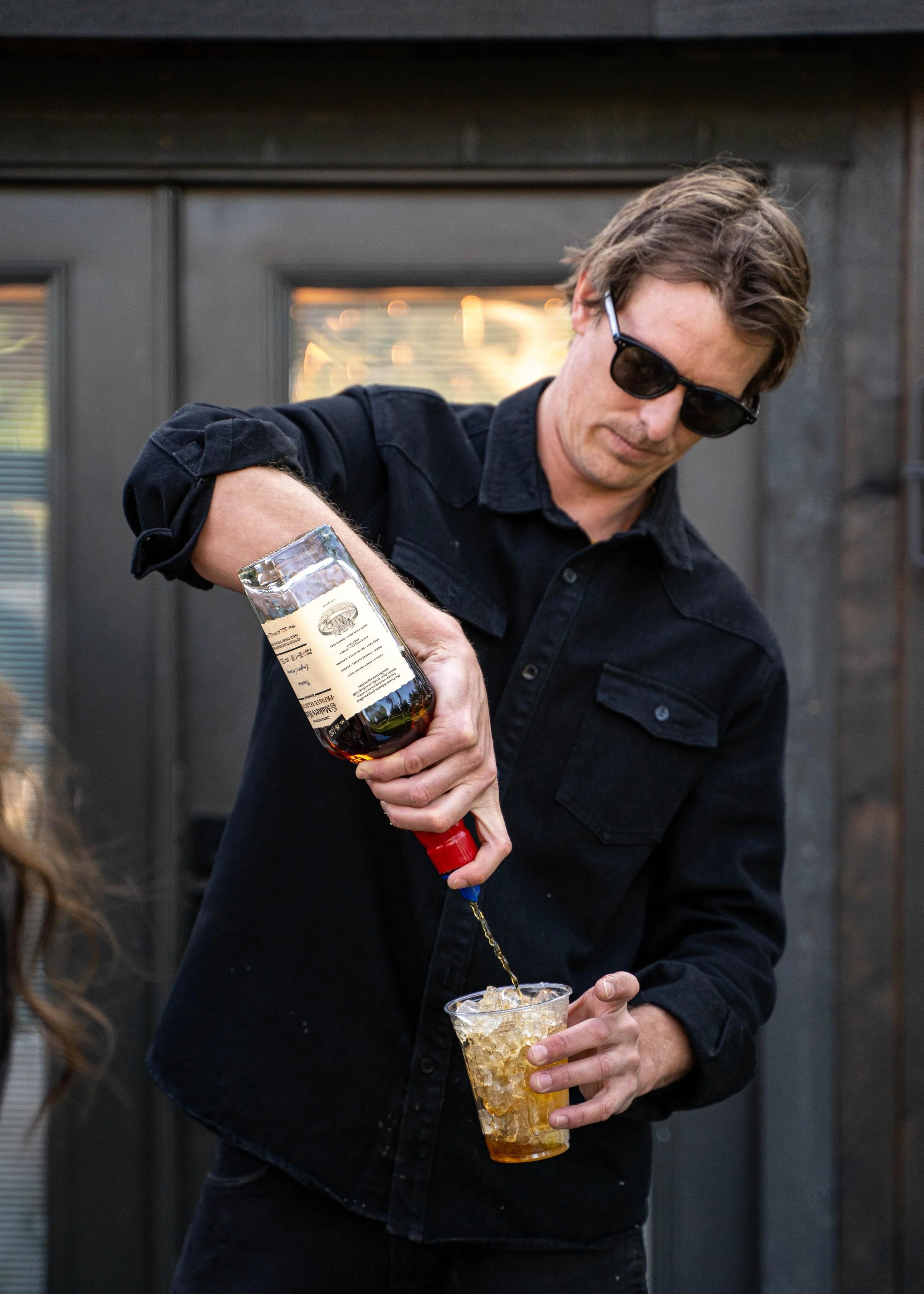 Cowboy wearing a black shirt and sunglasses pouring himself a drink over ice during a Montana Longhorn Ranch lifestyle photoshoot