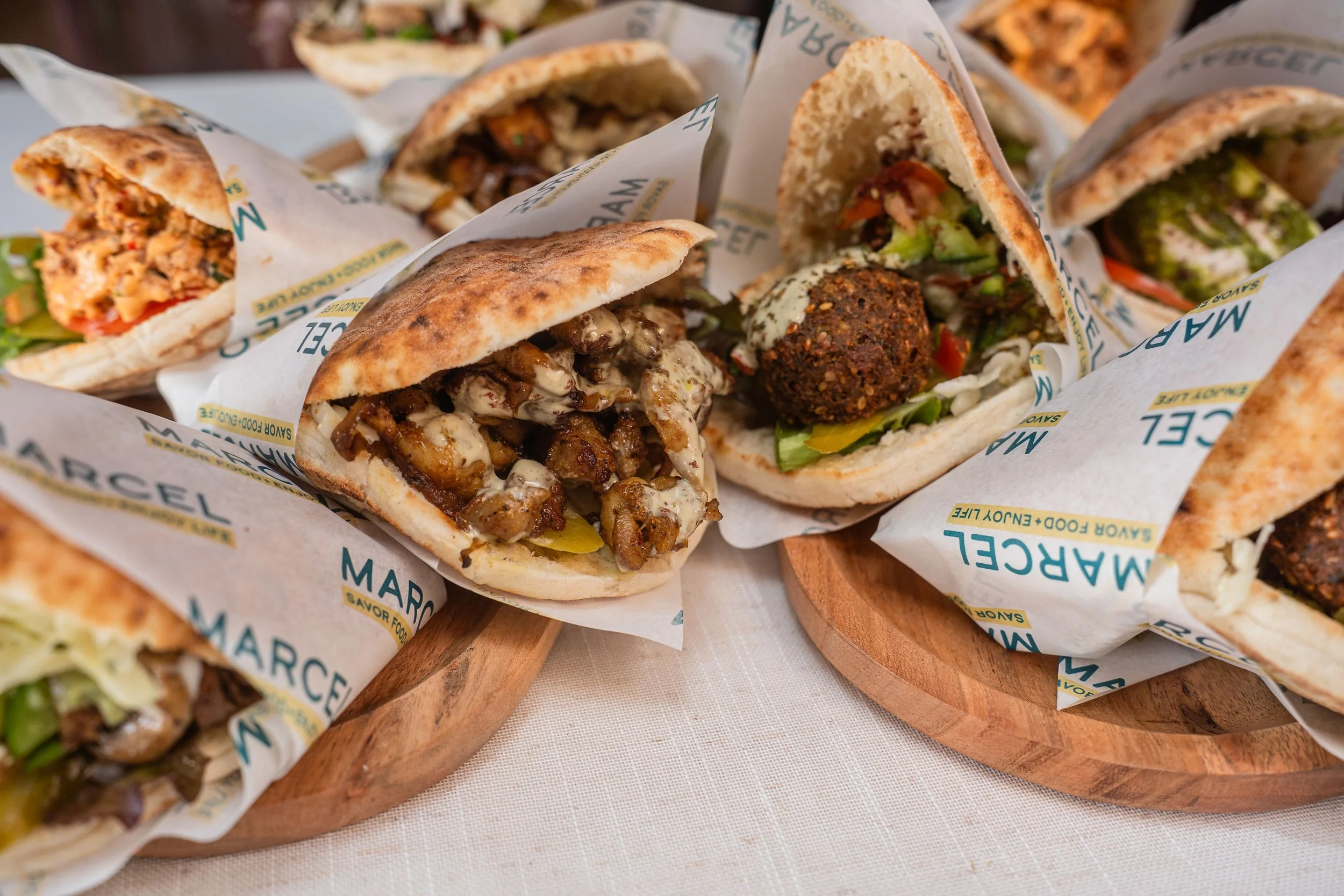 Assorted wrap sandwiches with various fillings, wrapped in branded paper, arranged on a wooden board.