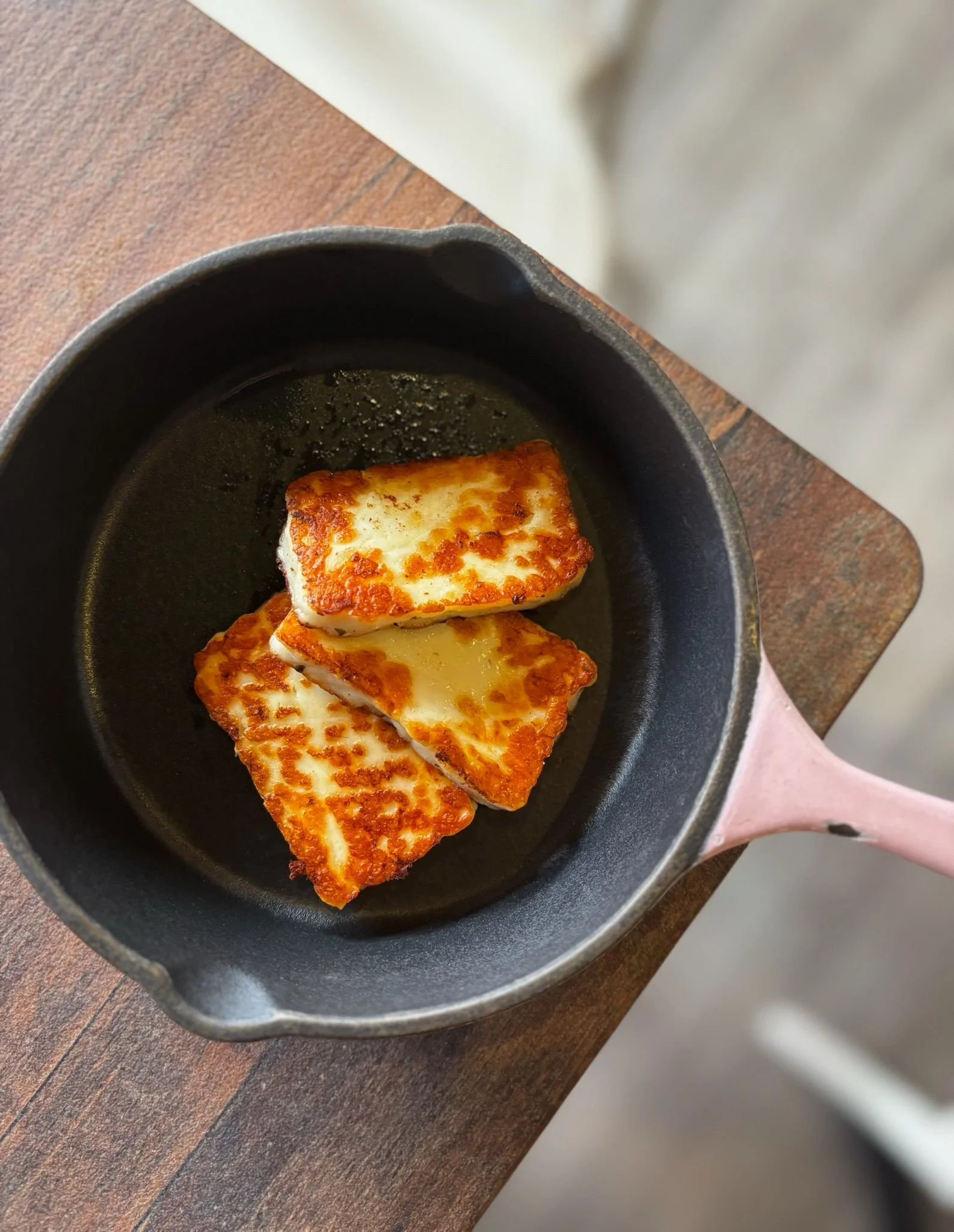 Fried cheese in a black cast iron skillet on a wooden table.