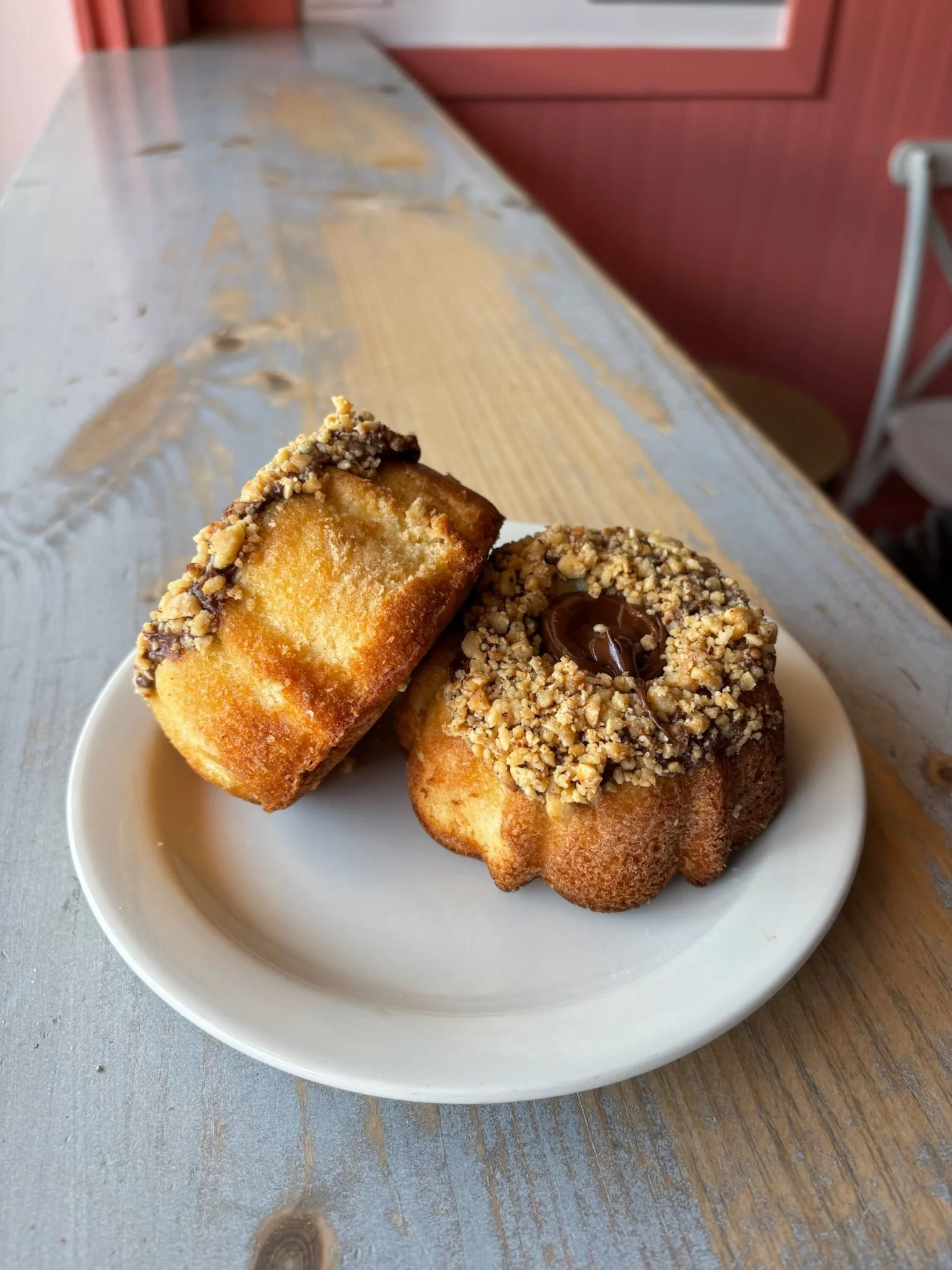 Close-up of three baked goods with chocolate and nuts on a white plate, placed on a wooden table.