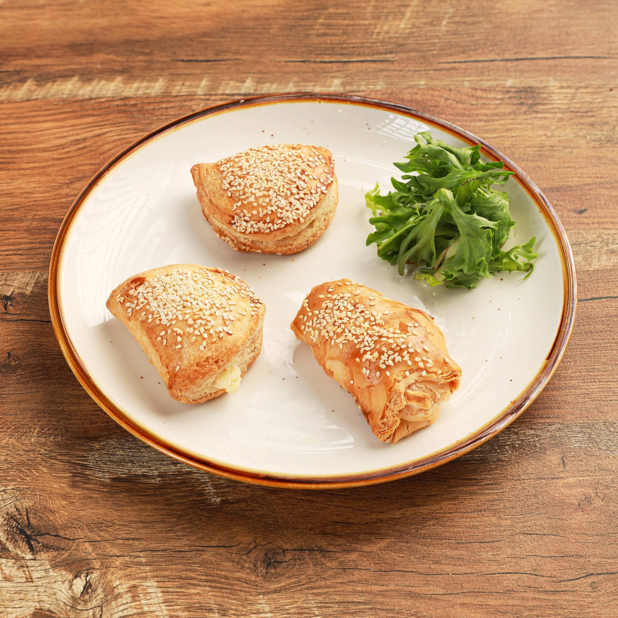 Close-up of a white plate with a sesame seed bun and some greens on a wooden table.