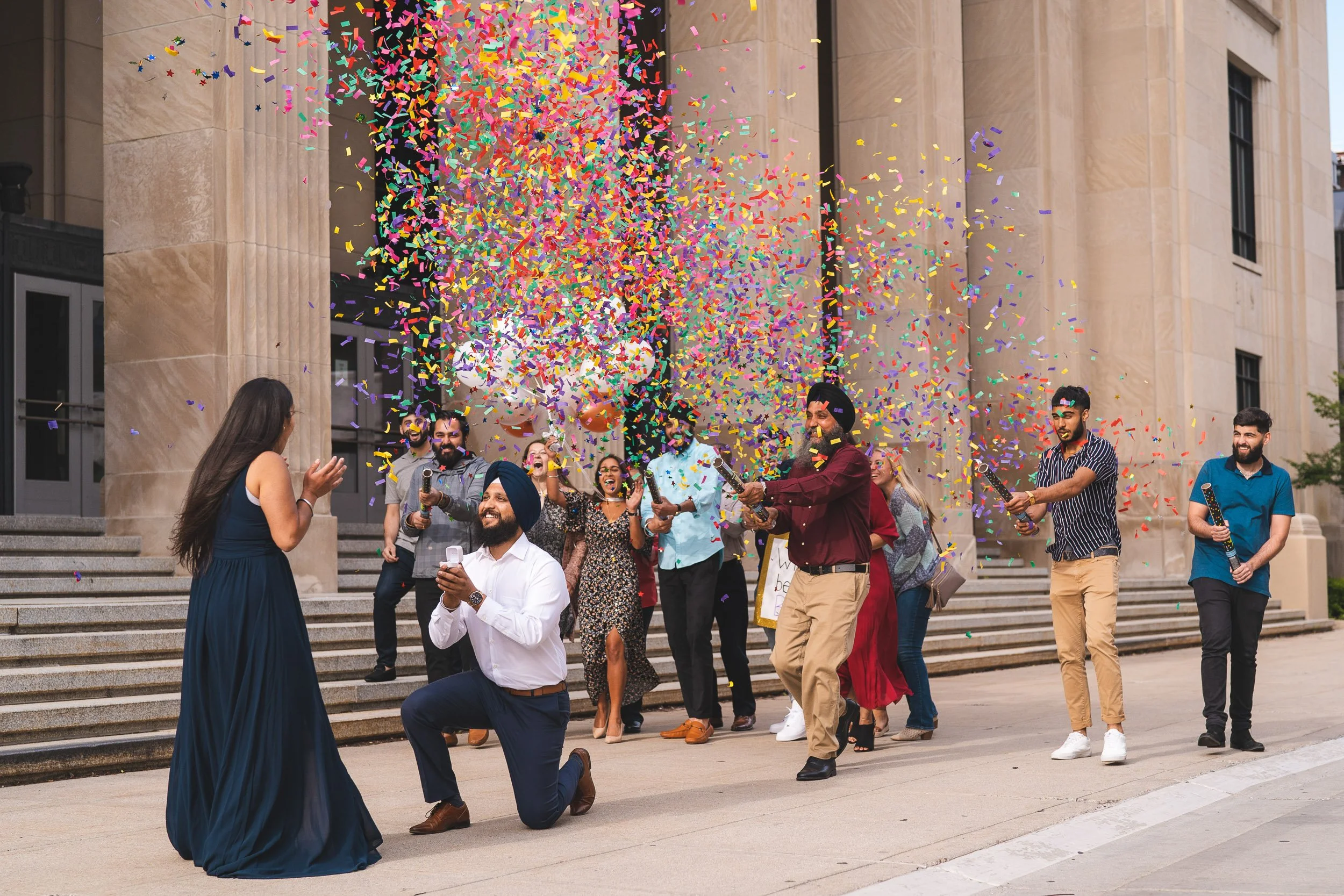 Man proposing to woman on courthouse steps with confetti and friends cheering