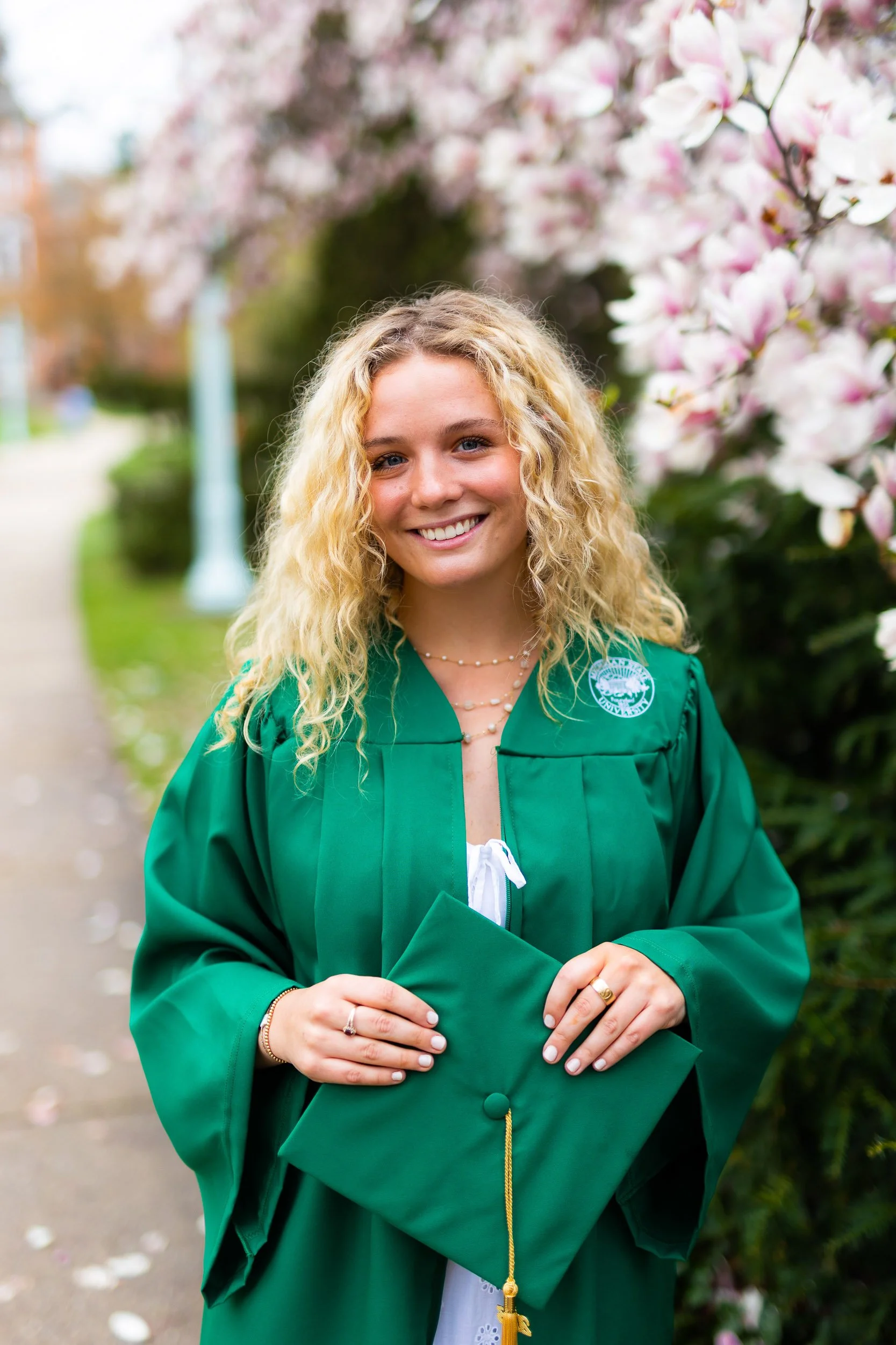 Senior girl in green graduation gown smiling near pink flowers