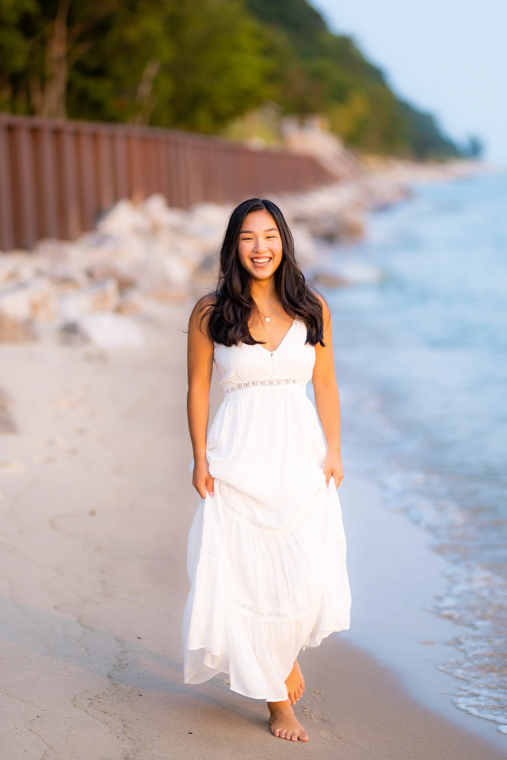 Woman in white dress smiling on lakeshore path