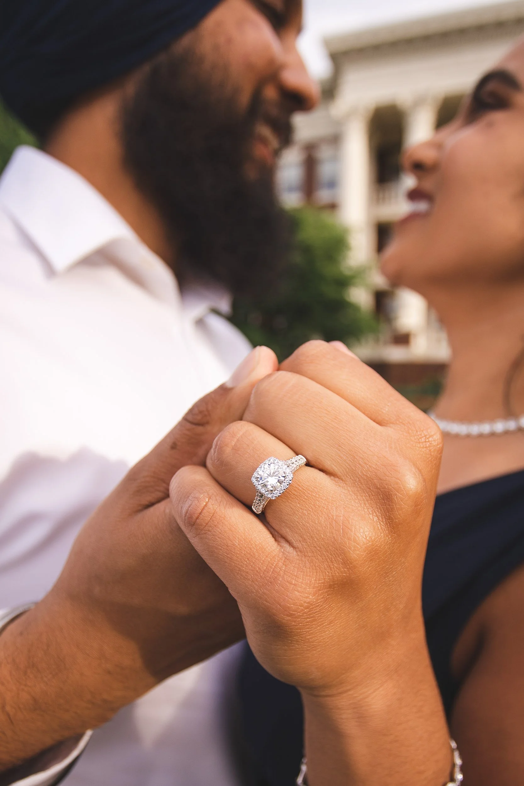 Close-up of engagement ring with couple embracing in background