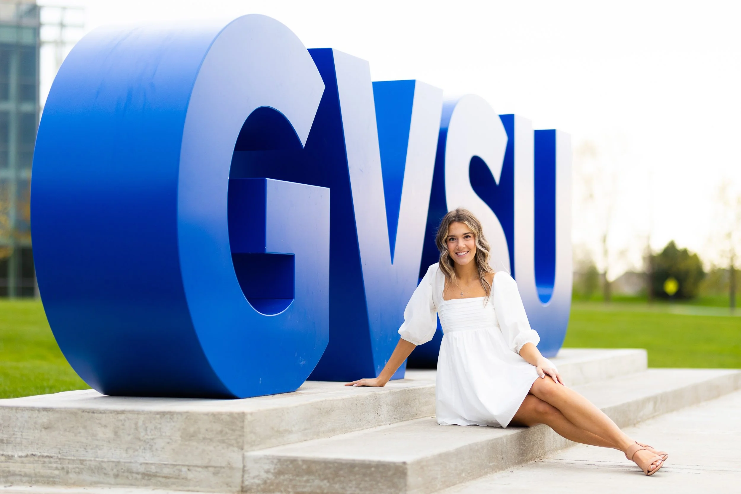 Senior portrait of woman sitting by GVSU sign in white dress