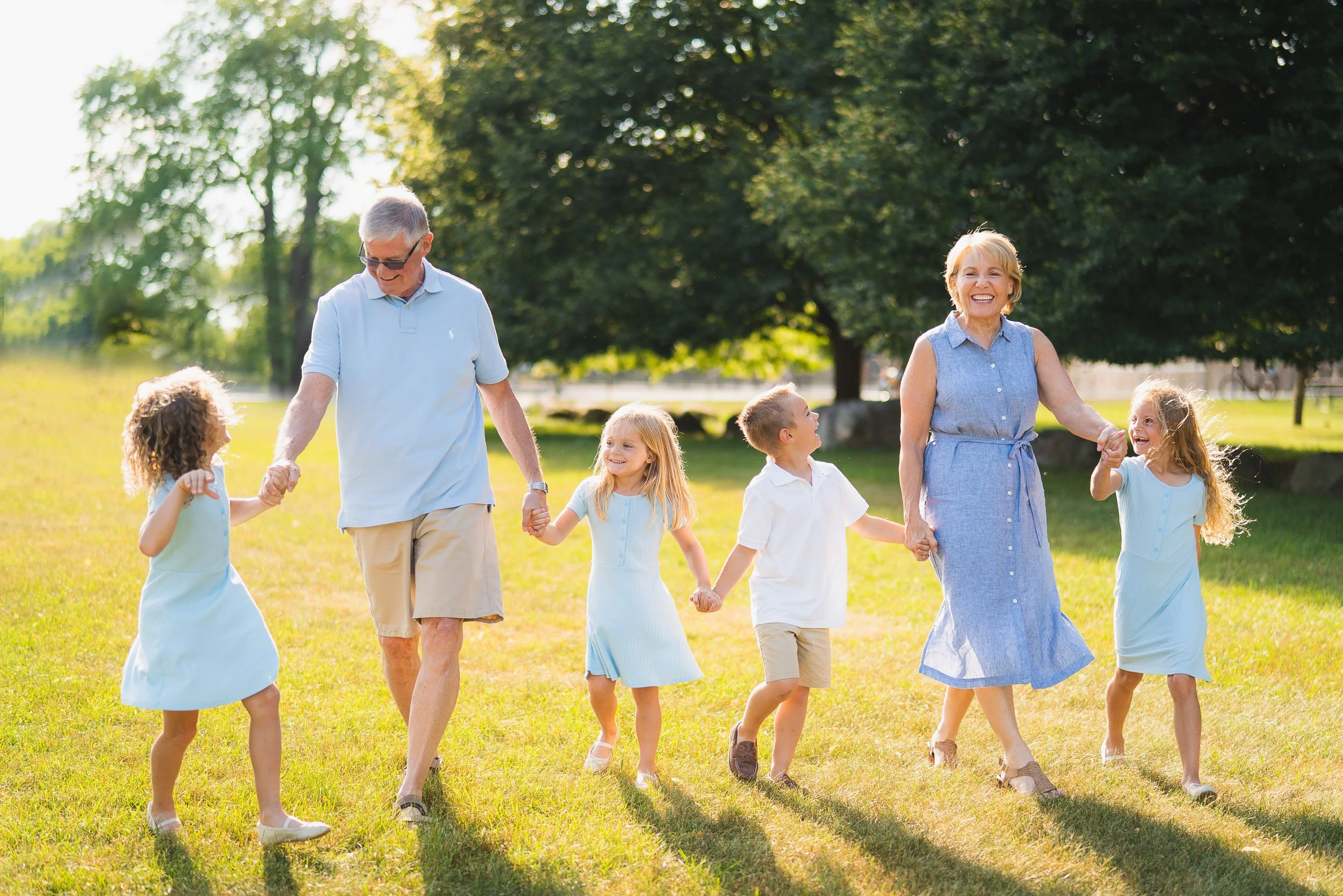 Family with young kids walking hand in hand through grassy field
