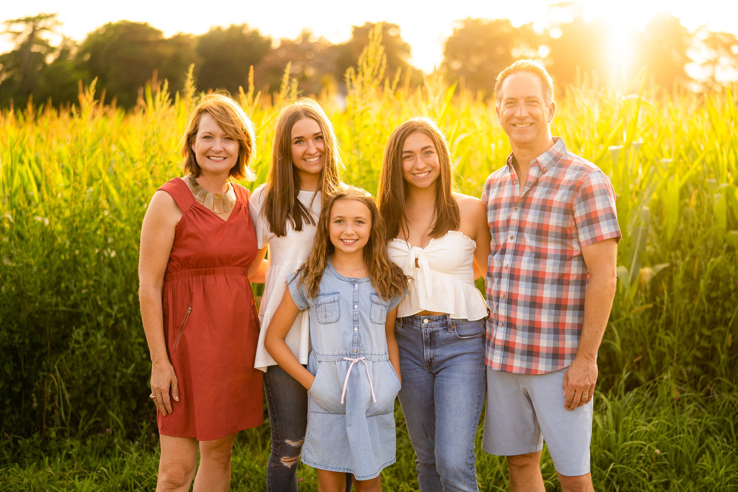 Family of five in summer outfits standing in cornfield