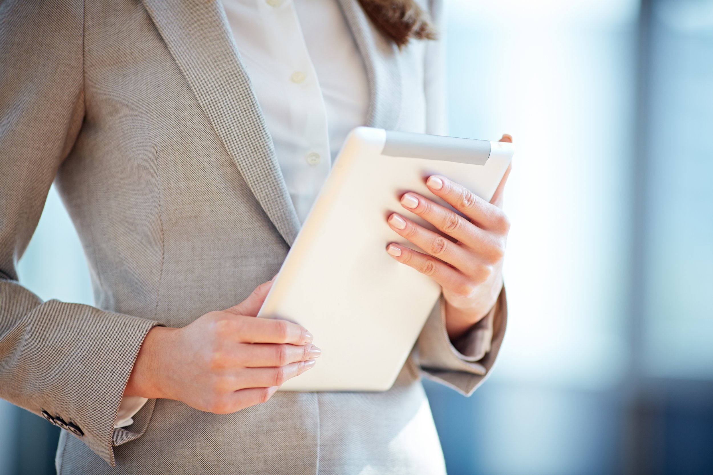 Woman in an Italian wool suit holding a tablet, standing confidently in a naturally lit office — representing professionalism, presence, and brand values.