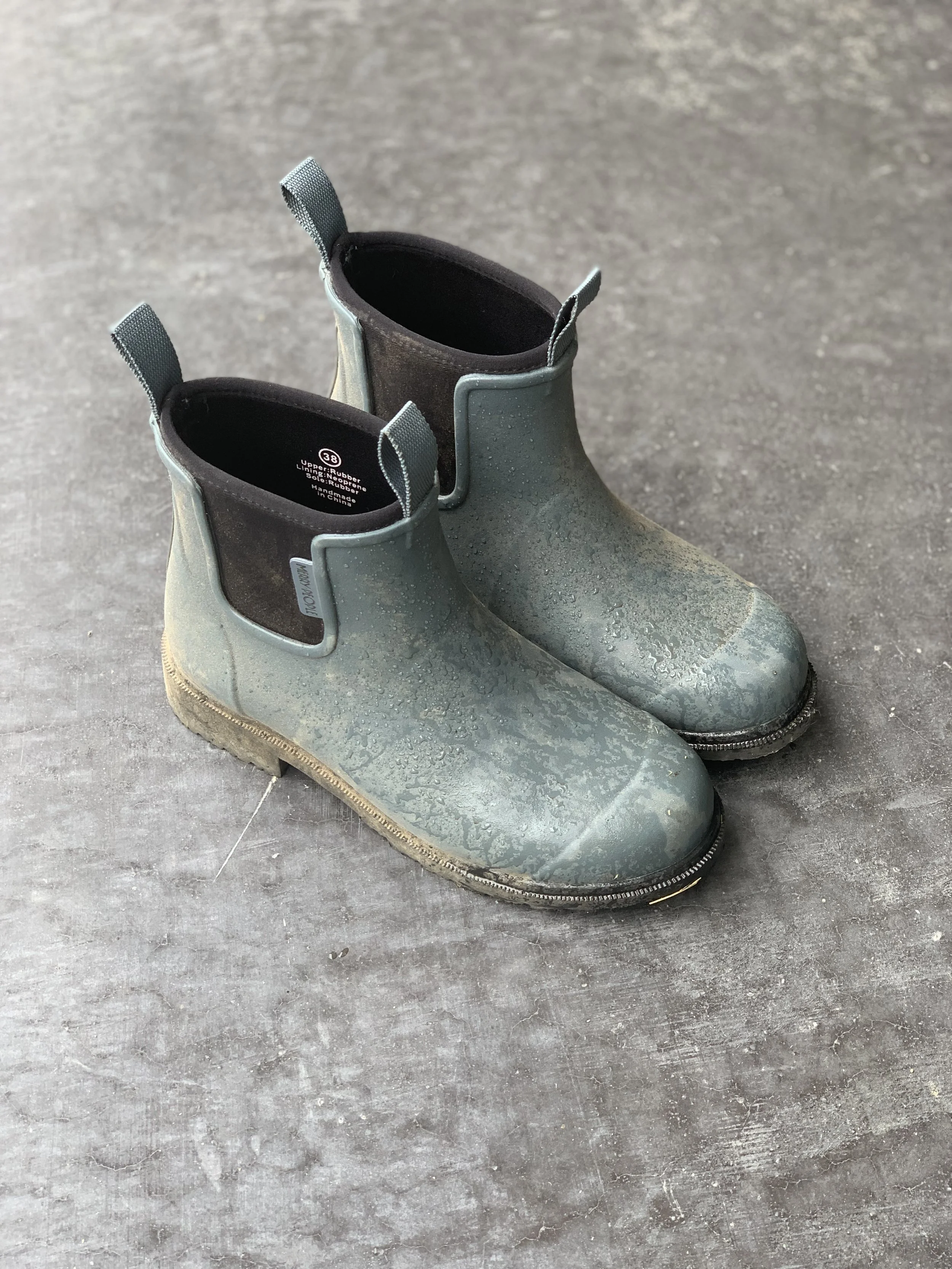 Pair of muddy green rubber rain boots on concrete surface.