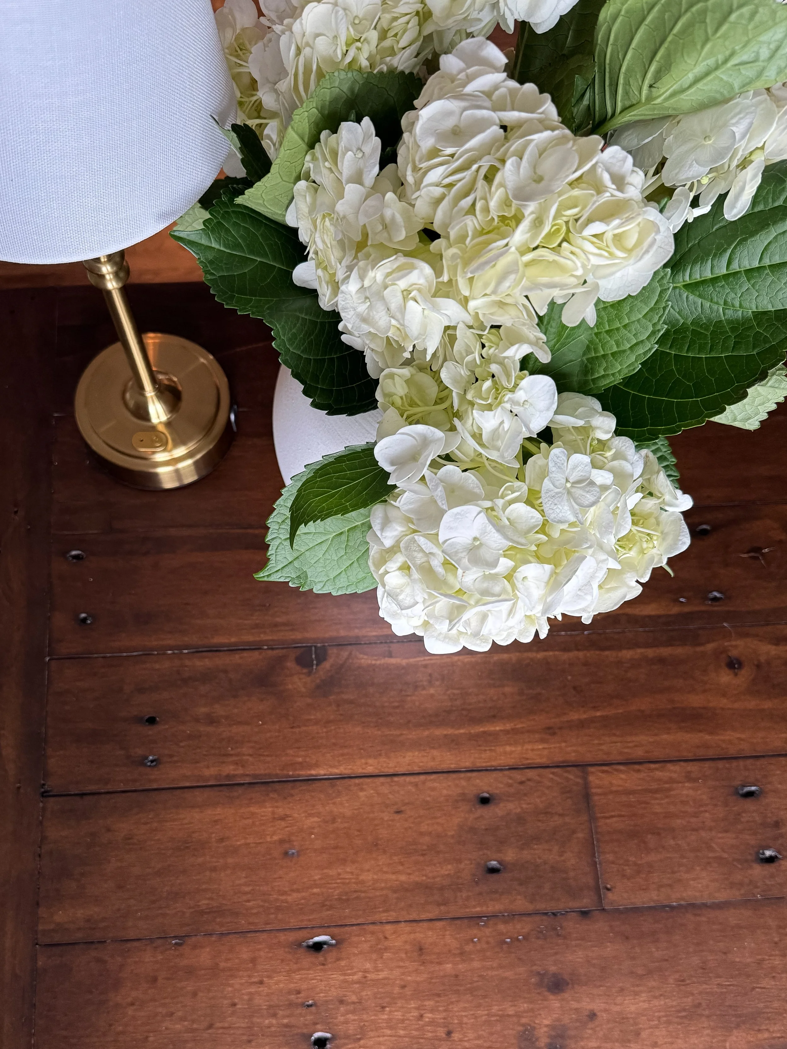 Detail Shot of Wooden Desk, Small Gold Lamp, and Hydrangea Flowers