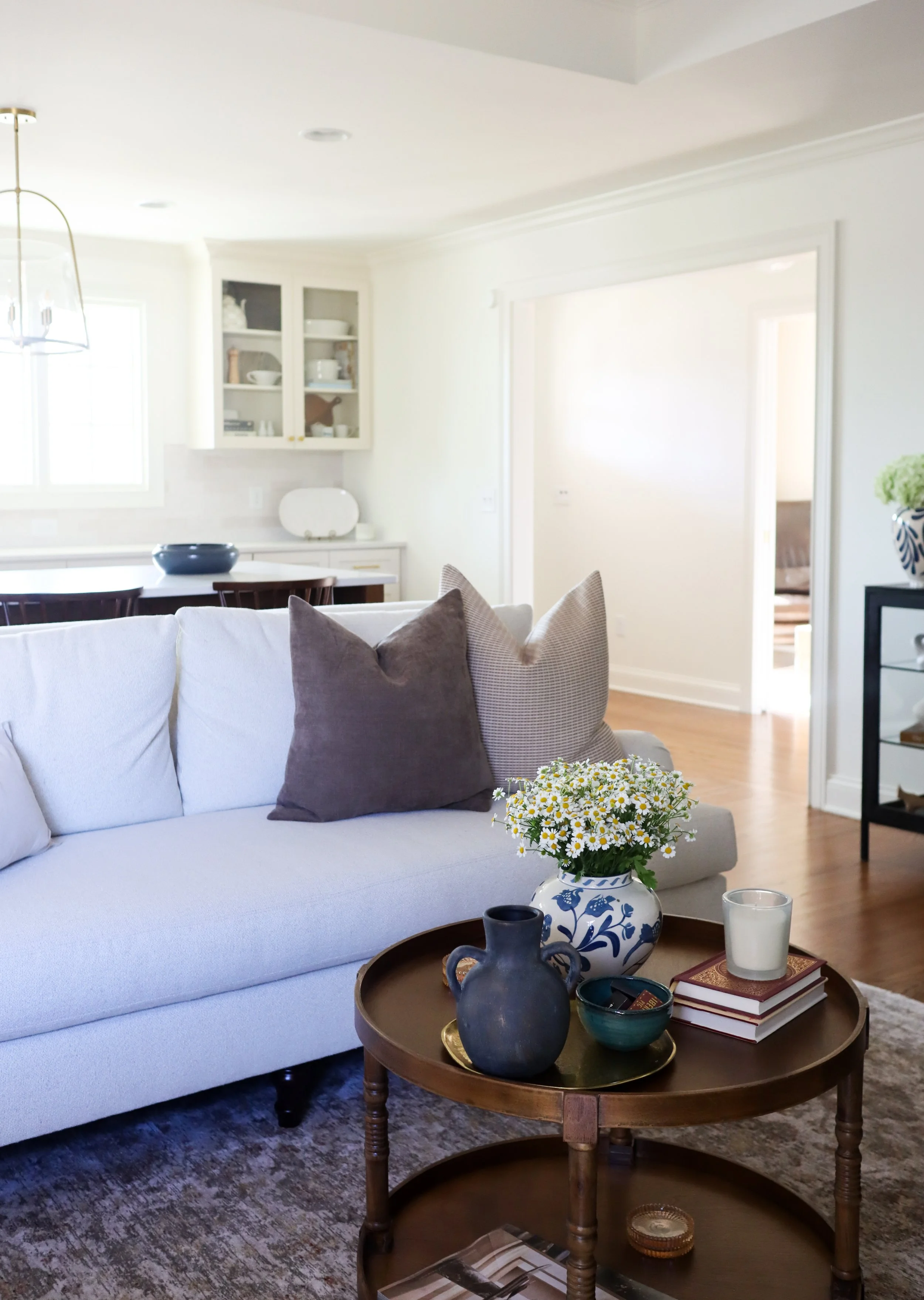 traditional neutral living room with cream couch, brown and tan pillows, wooden side table, kitchen with cream cabinets and wooden island in the background