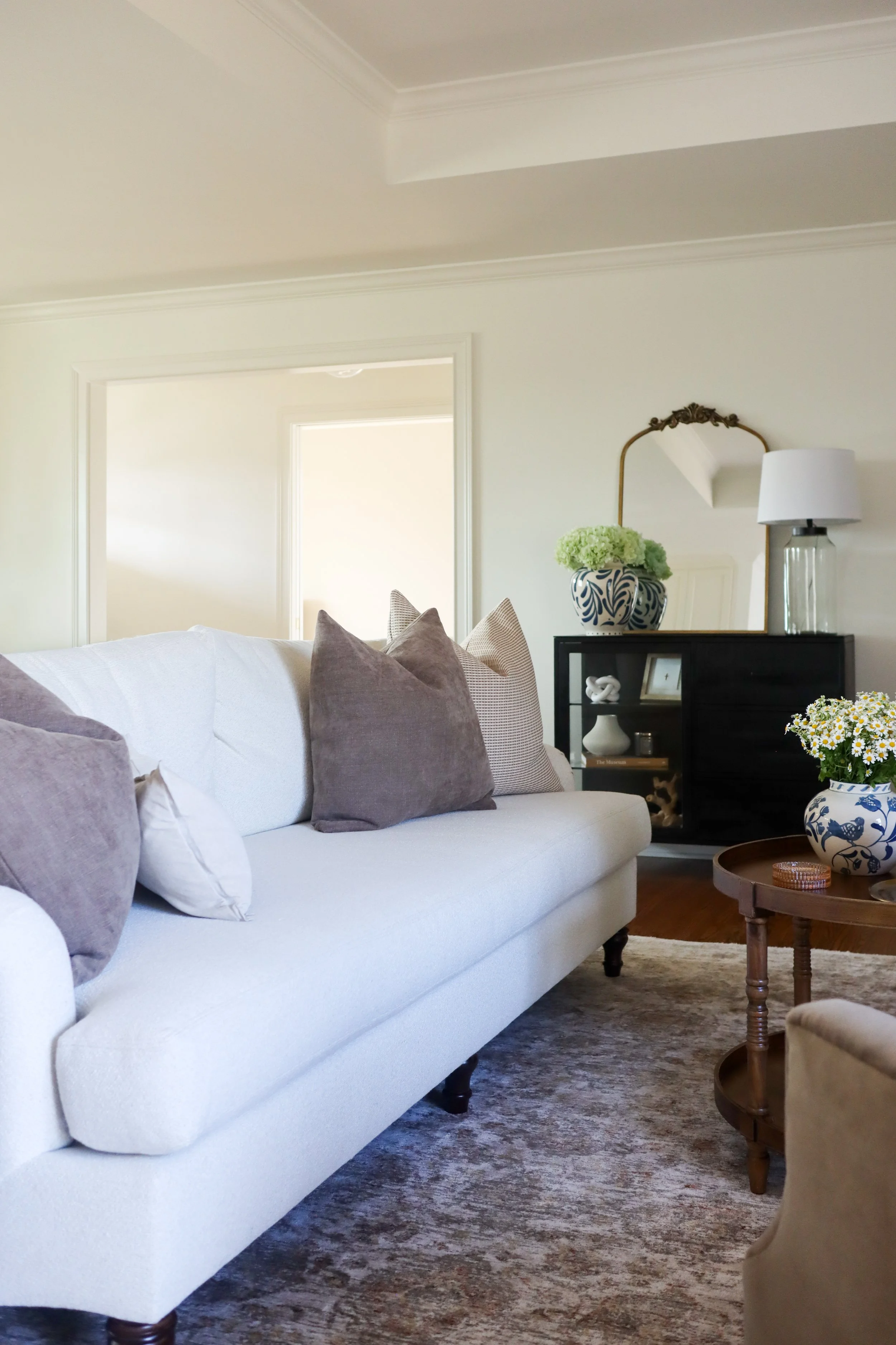 cream couch, brown and tan textured pillows, black console, vintage brass mirror, blue and white vases, large lamp, wooden coffee table