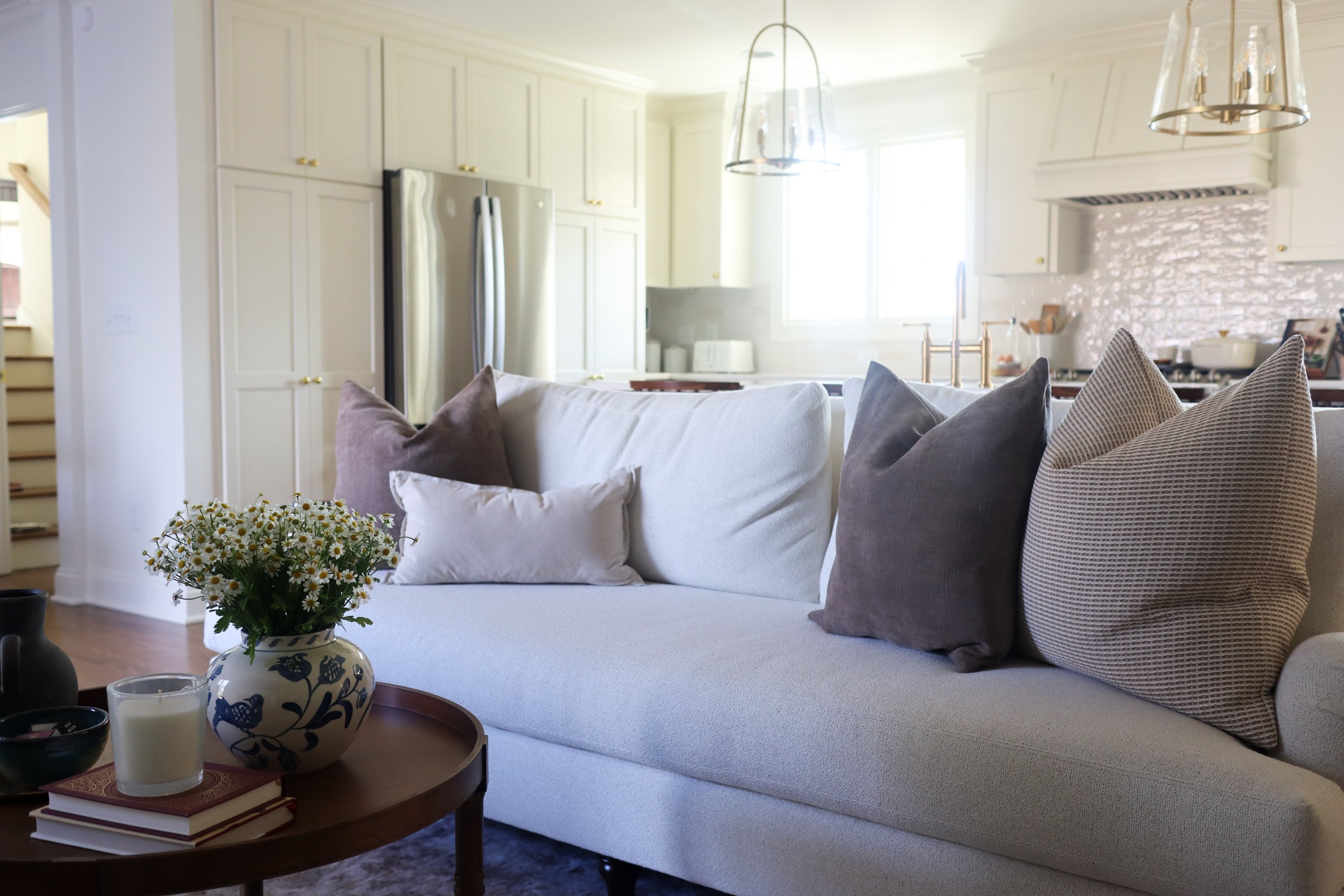 traditional neutral living room with cream couch, brown and tan pillows, wooden side table, kitchen with cream cabinets and wooden island in the background