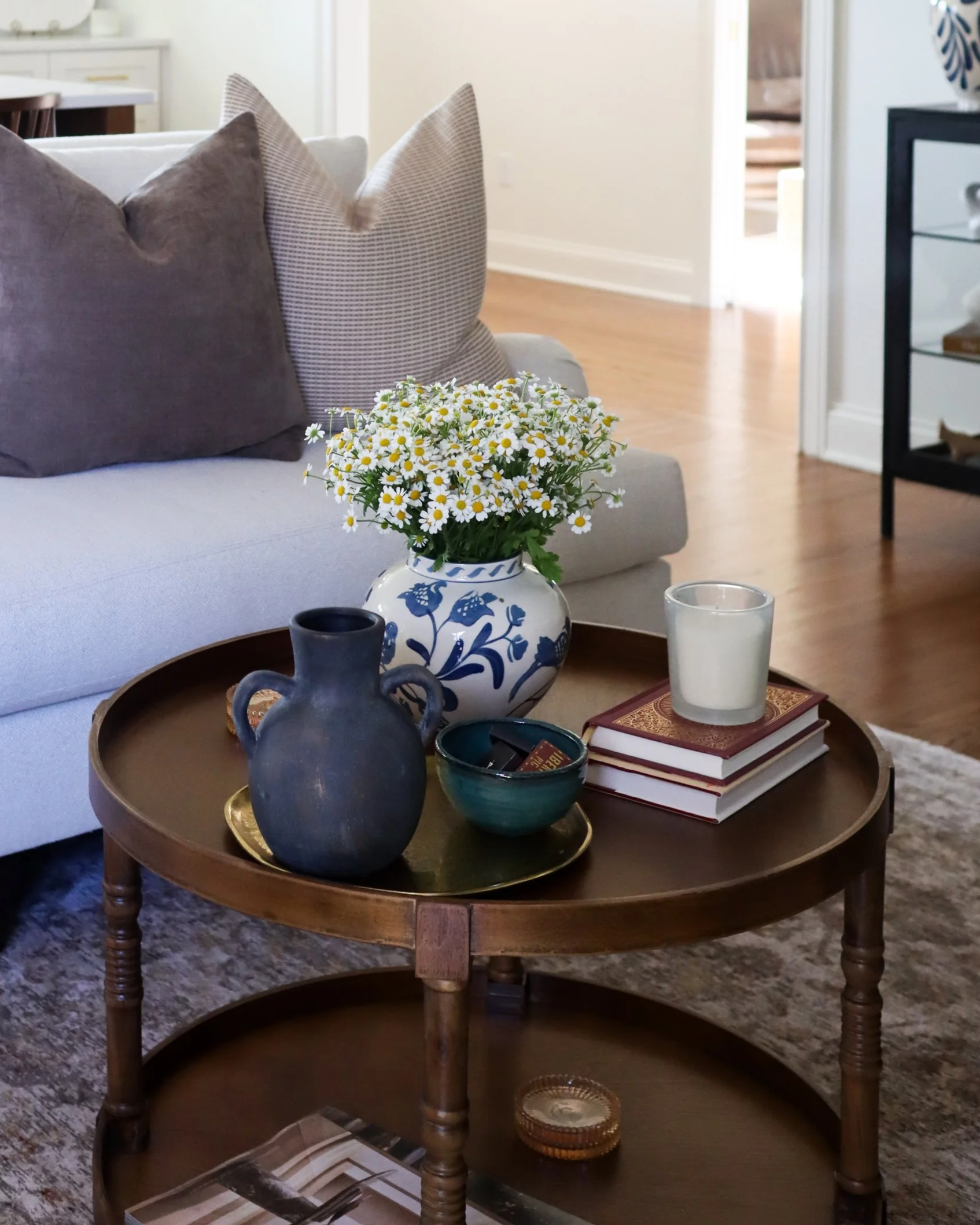 wooden coffee table with blue and cream vase, grey vase, coffee table books and candle. couch in background with brown and tan textured pillows