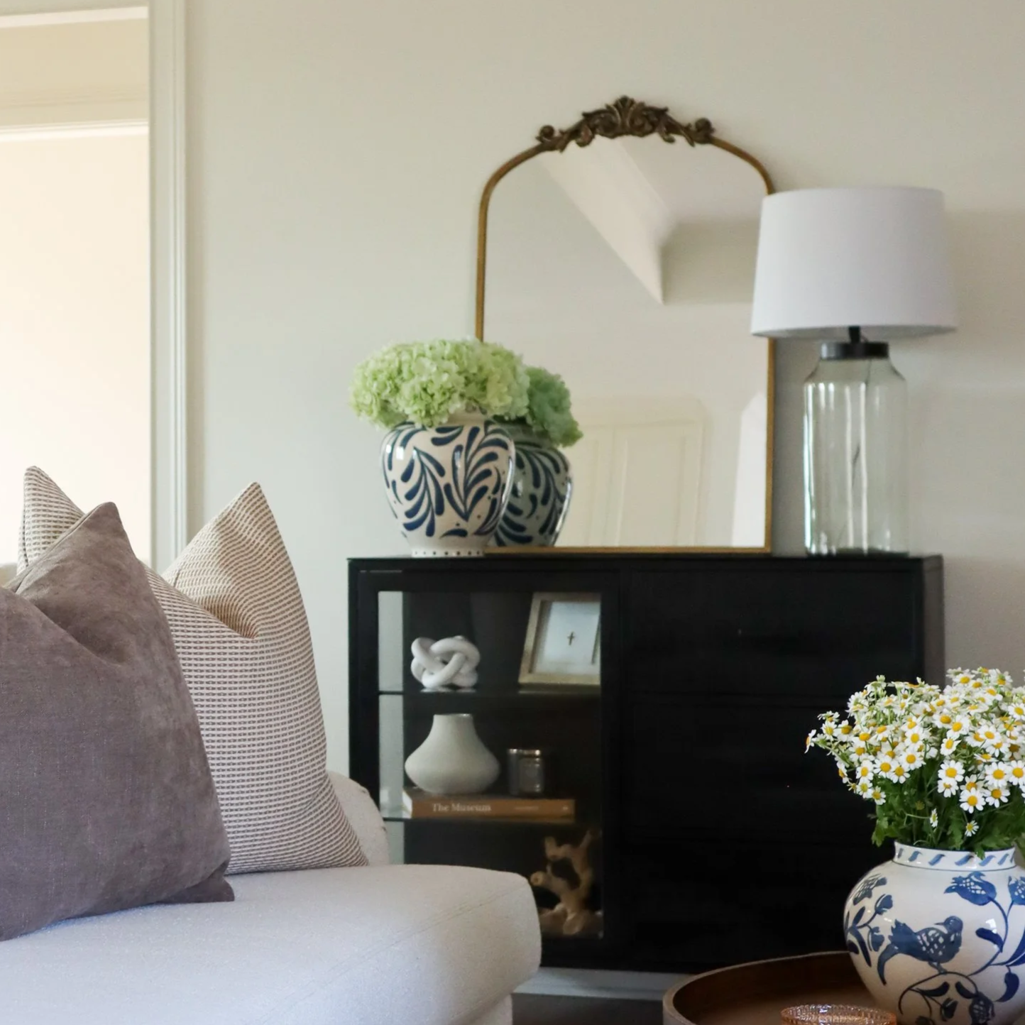 cream couch, brown and tan textured pillows, black console, vintage brass mirror, blue and white vases, large lamp, wooden coffee table