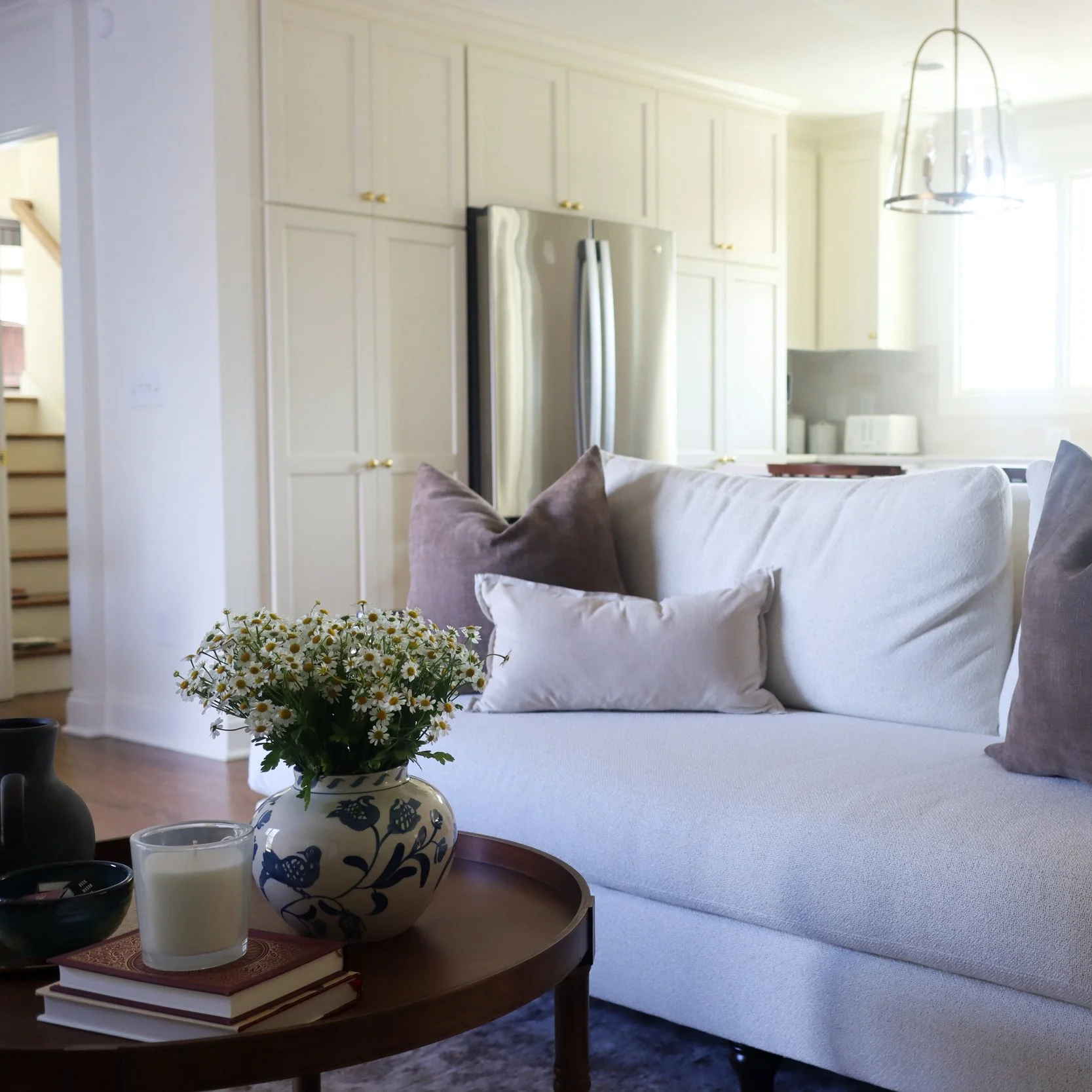 traditional neutral living room with cream couch, brown and tan pillows, wooden side table, kitchen with cream cabinets and wooden island in the background