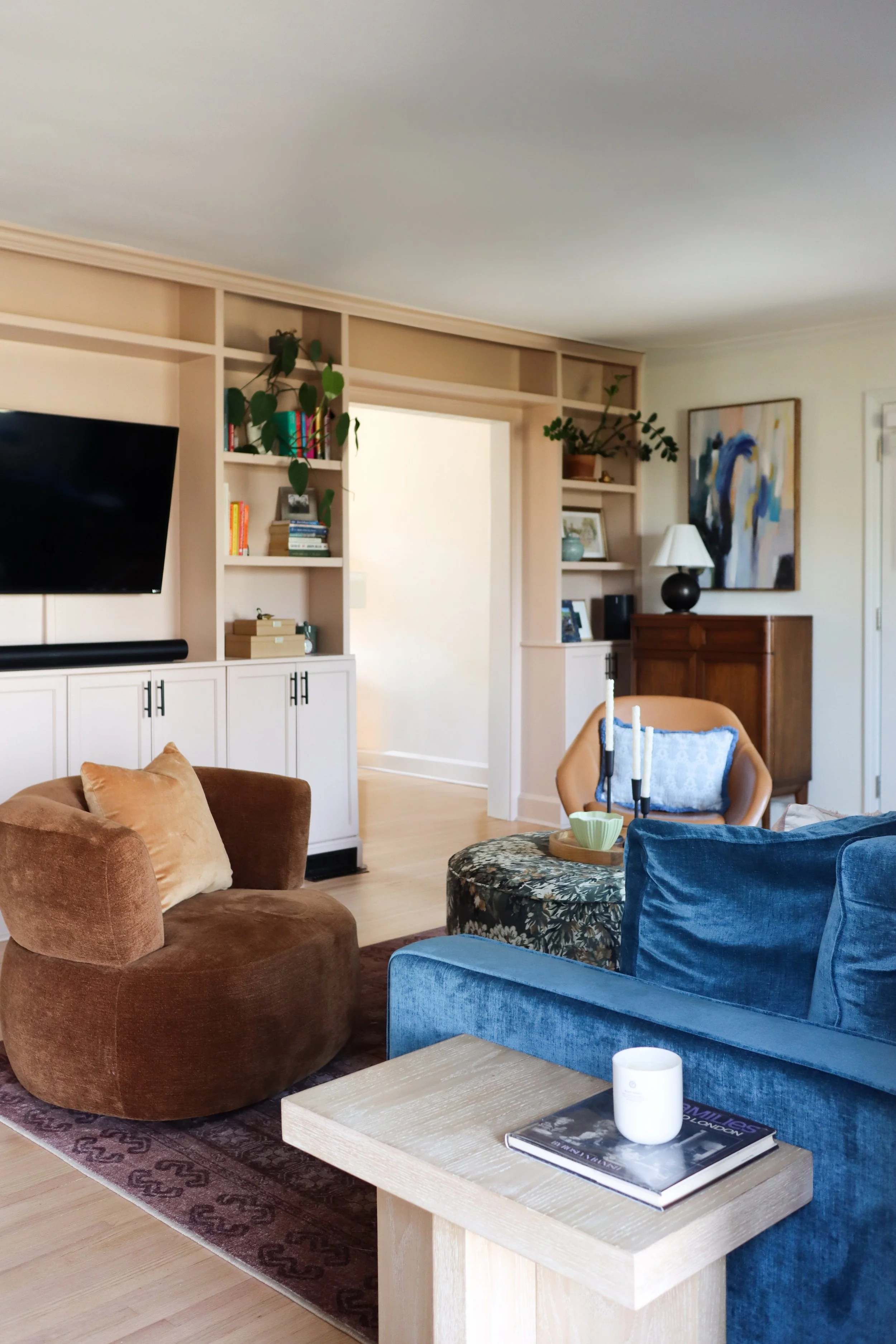 Jewel-toned living room featuring deep blue and green upholstery, warm wood tones, and custom built-in cabinetry