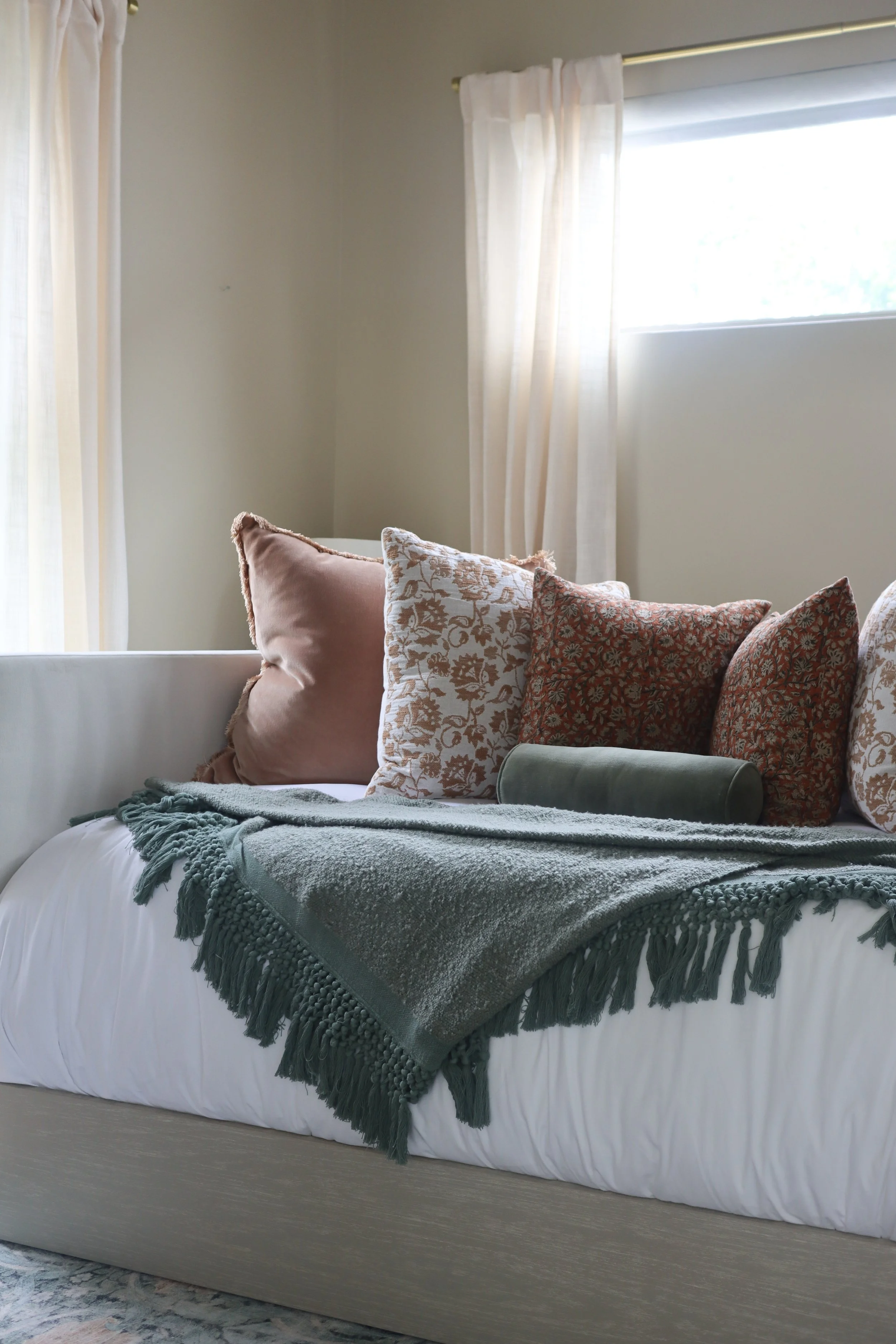 Cozy guest room featuring a trundle bed layered with soft green and rust-colored bedding.