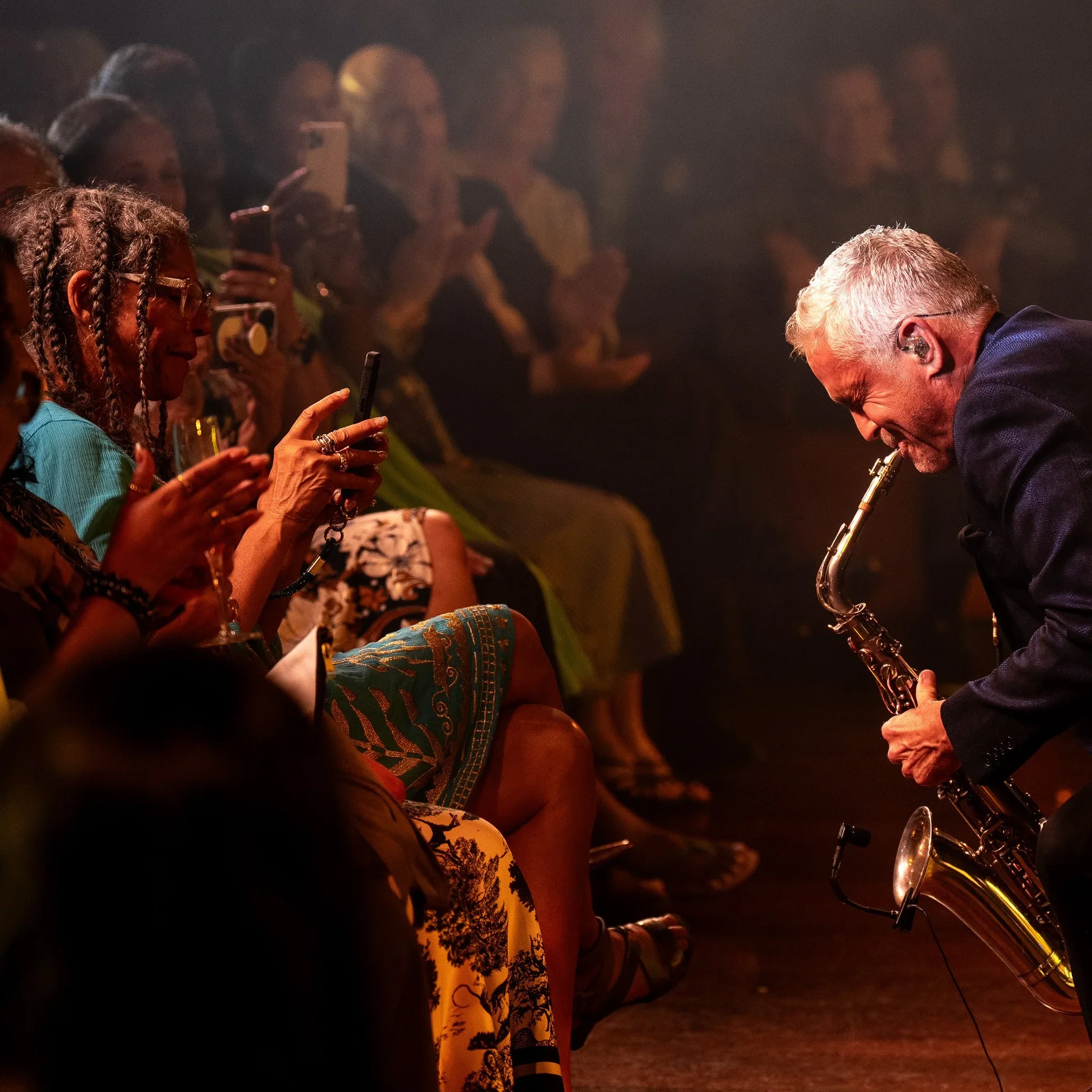 Dave Koz performing on stage in front of an audience, with concertgoers taking photos and videos.