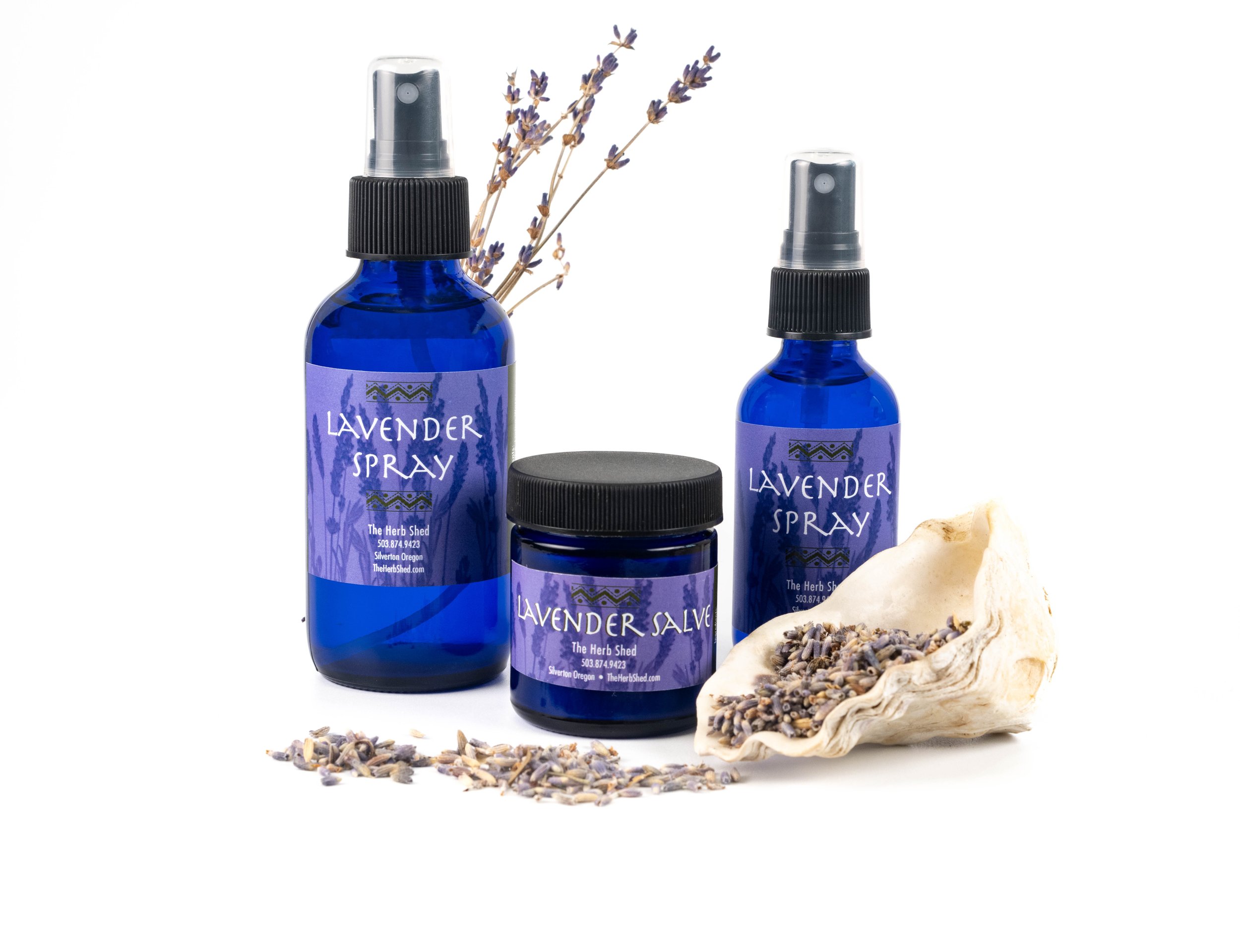 Blue bottles labeled lavender spray and lavender salve, dried lavender in a shell, and loose lavender flowers.