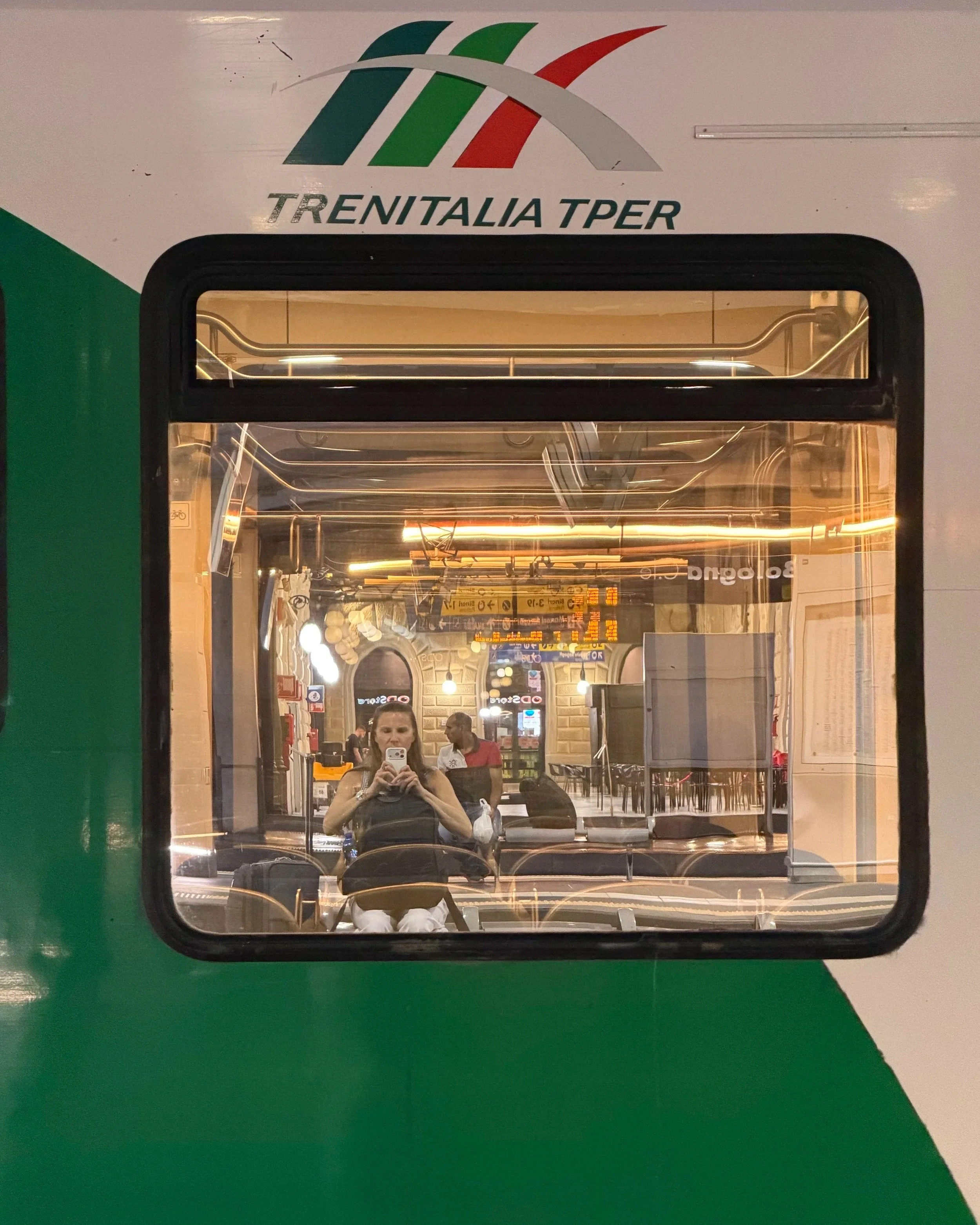 Reflection selfie in a Trenitalia TPER train window at Bologna Centrale station in the early morning.