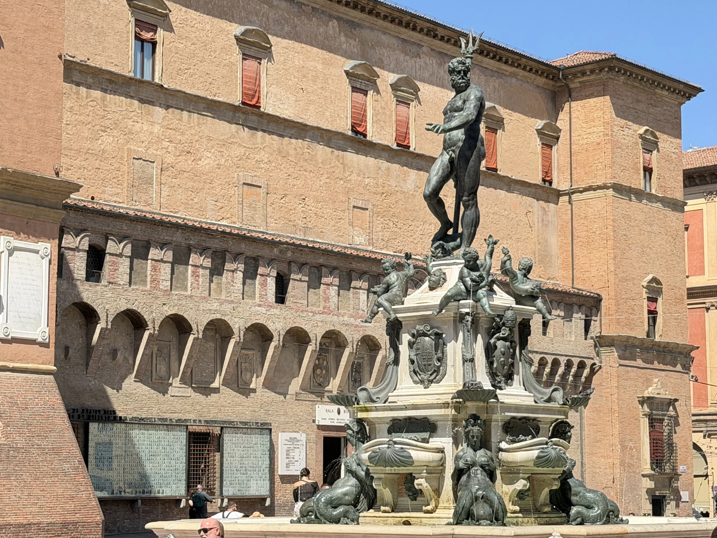 Bronze statue of Neptune atop a stone fountain in a Bologna piazza, surrounded by historic buildings.