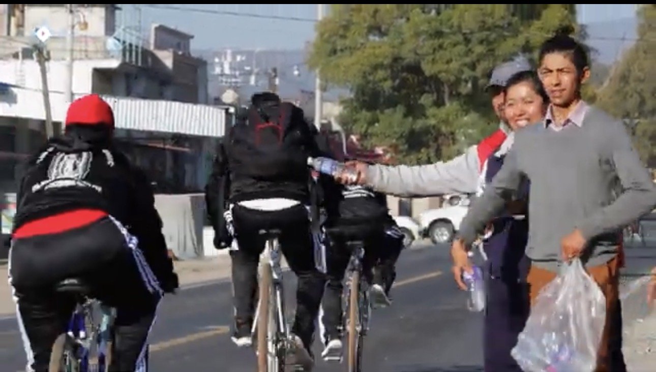 People riding bikes and another person handing out water bottles on a city street.