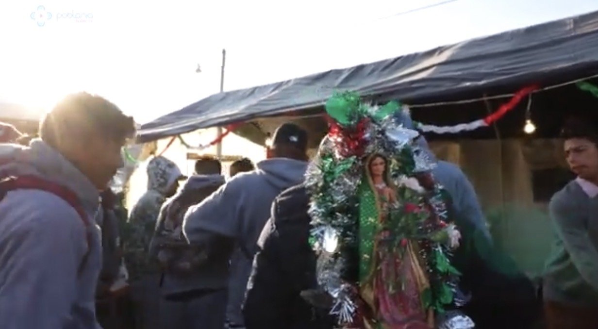 People at a marketplace or outdoor event with a religious or cultural figure in traditional attire, surrounded by a makeshift canopy, during late afternoon or evening.