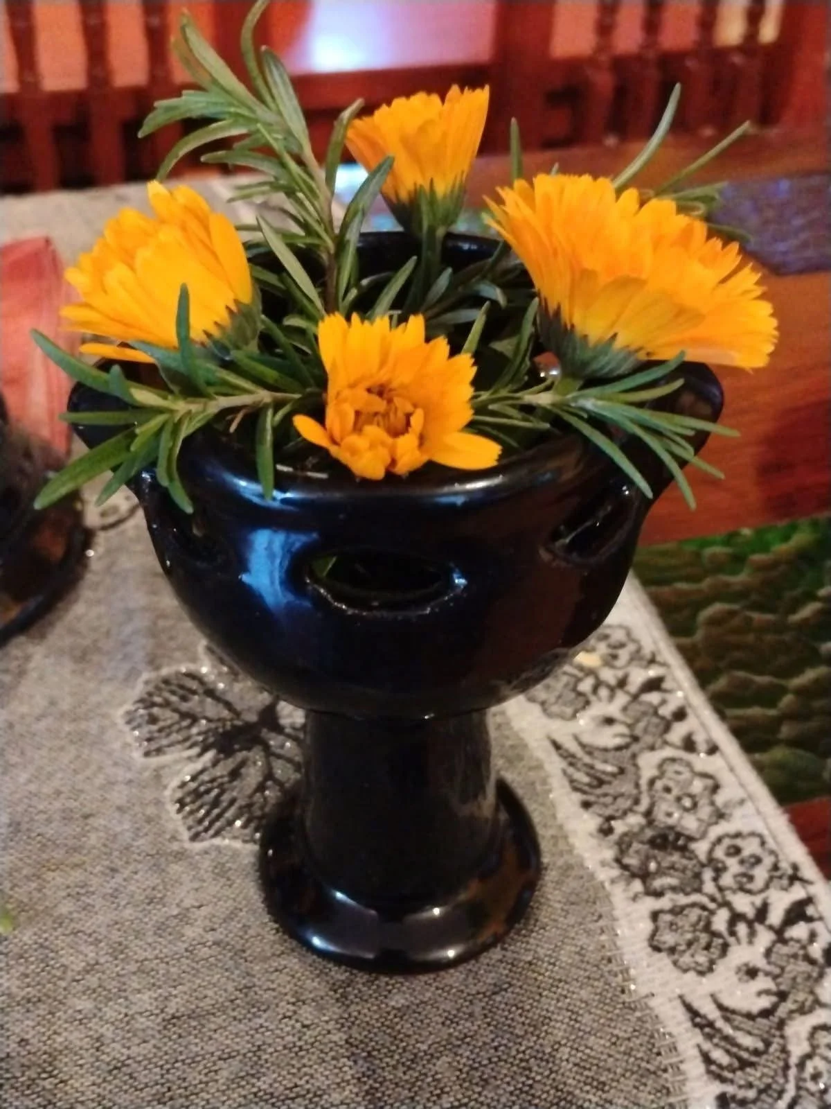 Yellow flowers in a black vase on a gray embroidered tablecloth.