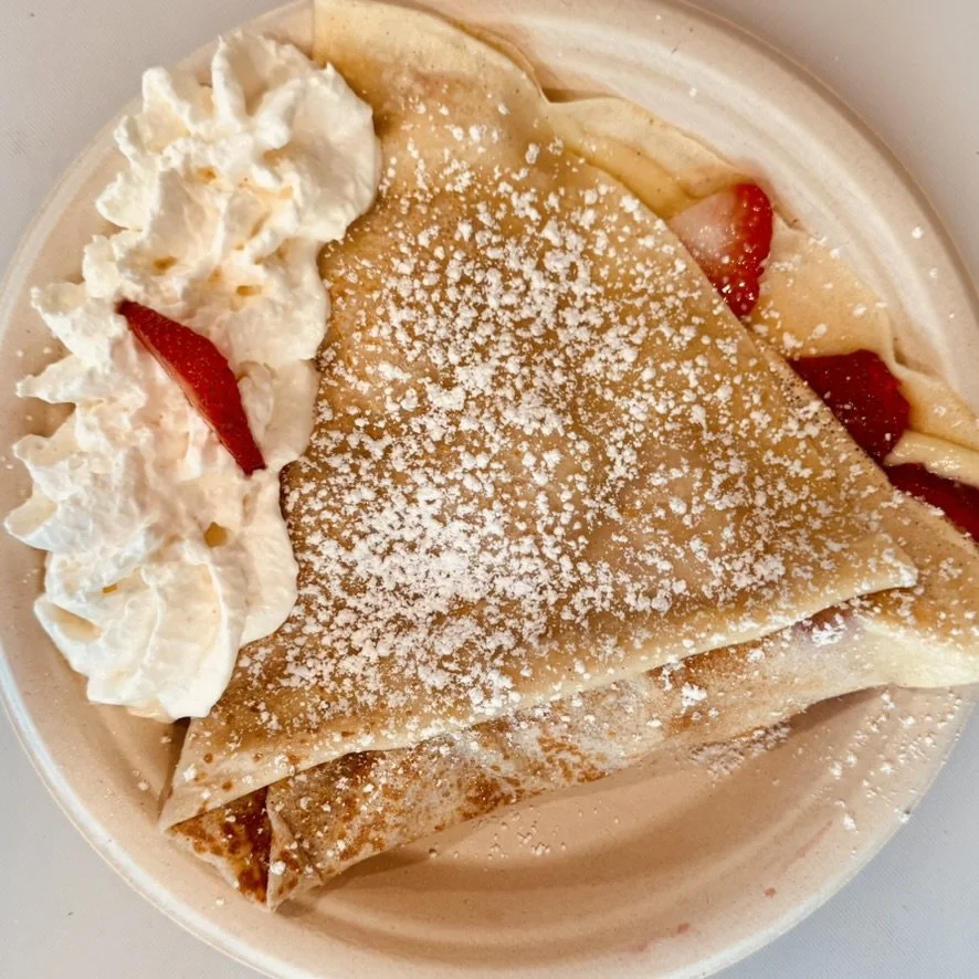 Crepe with powdered sugar, whipped cream, and strawberries in a bowl.