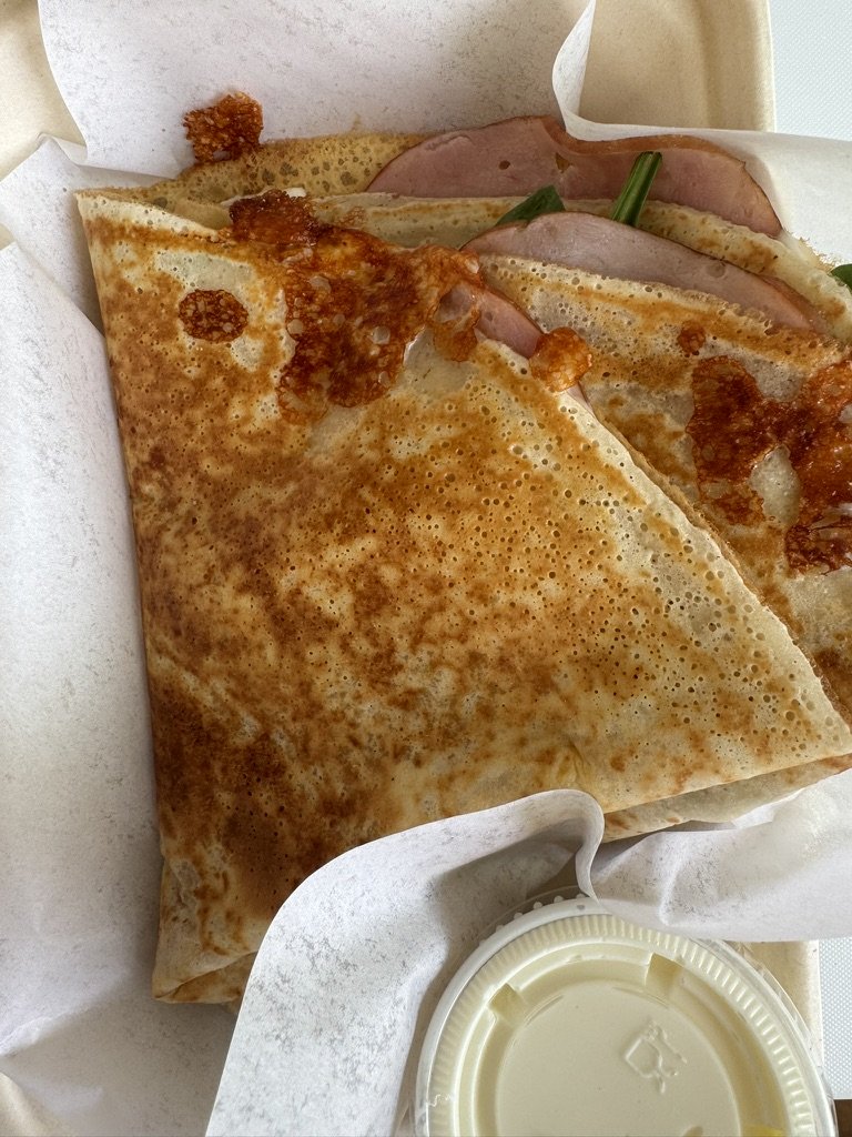 A folded crepe with bacon, green onions, and shredded cheese inside, served with a side of dipping sauce.