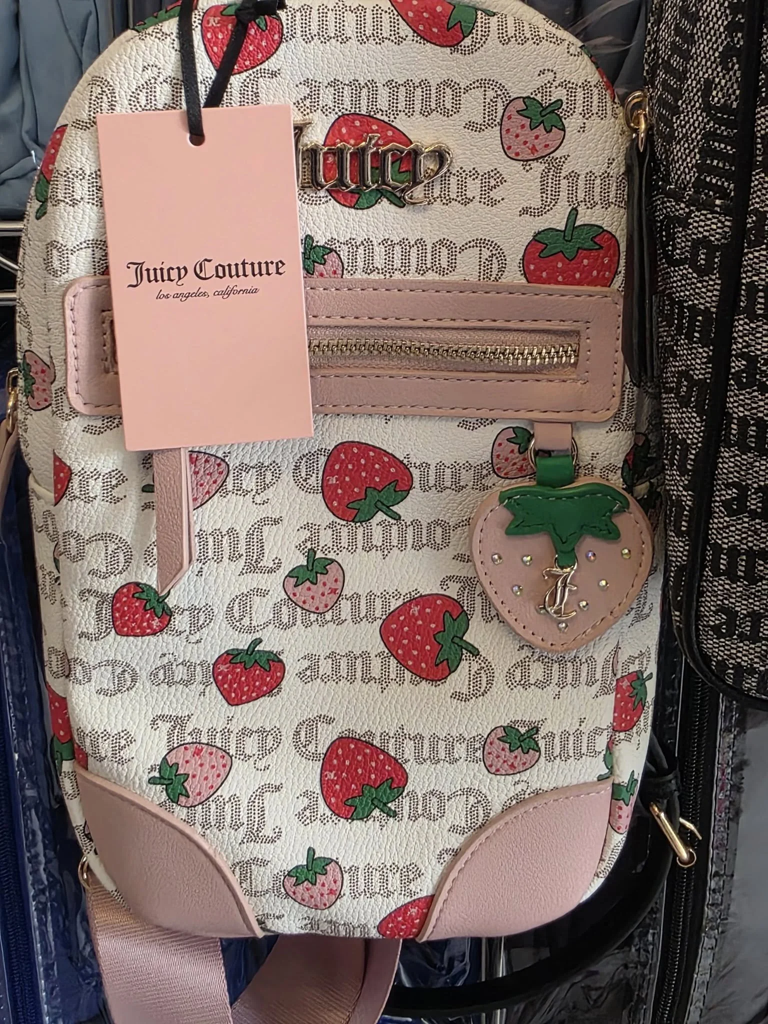A strawberry-themed Juicy Couture backpack with pink leather accents and a strawberry-shaped tag, featuring multiple strawberries and the Juicy Couture logo in a repeating pattern.