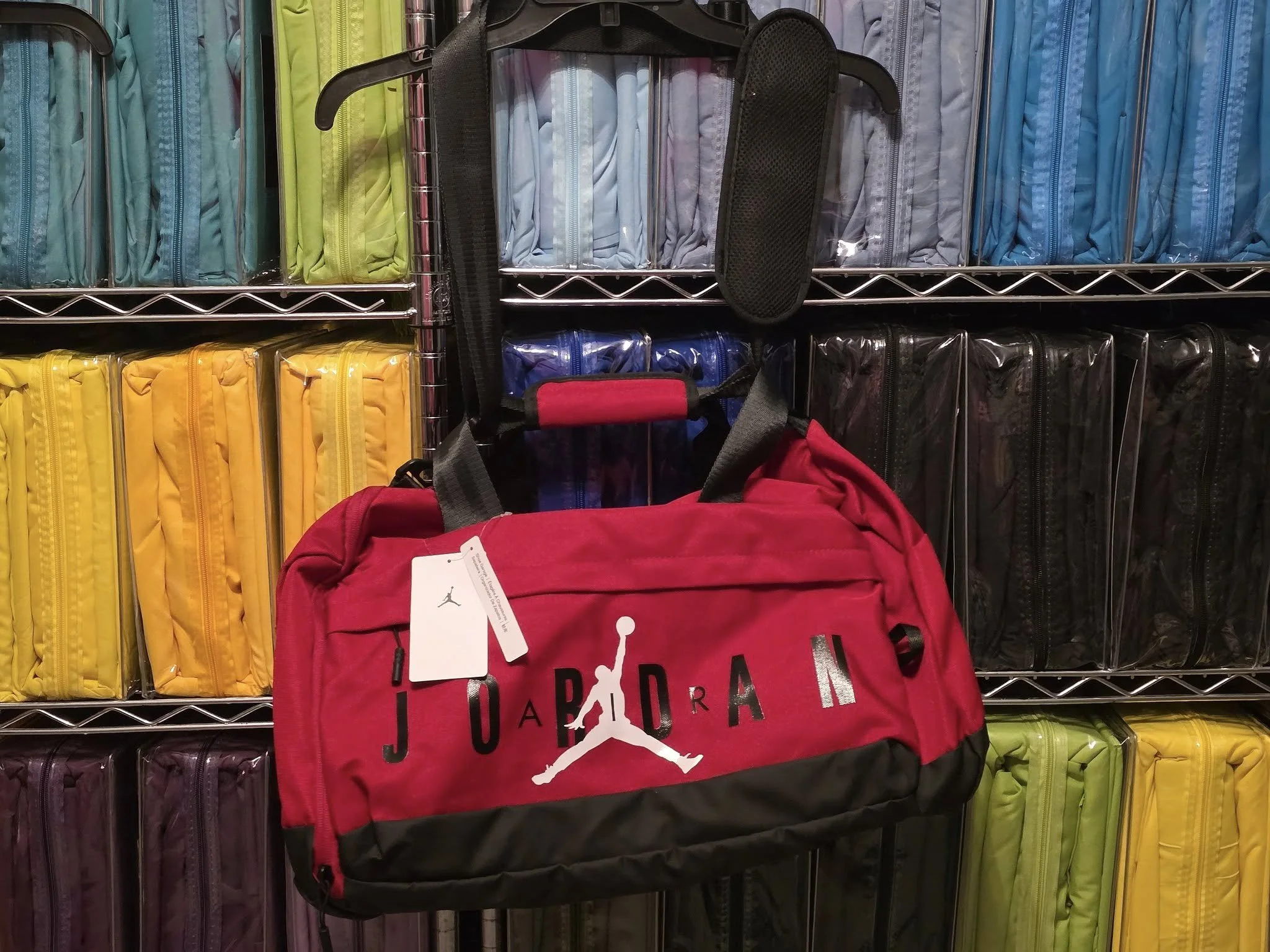 Red Jordan basketball duffel bag hanging on a metal shelf, surrounded by colorful backpacks in yellow, purple, blue, and black