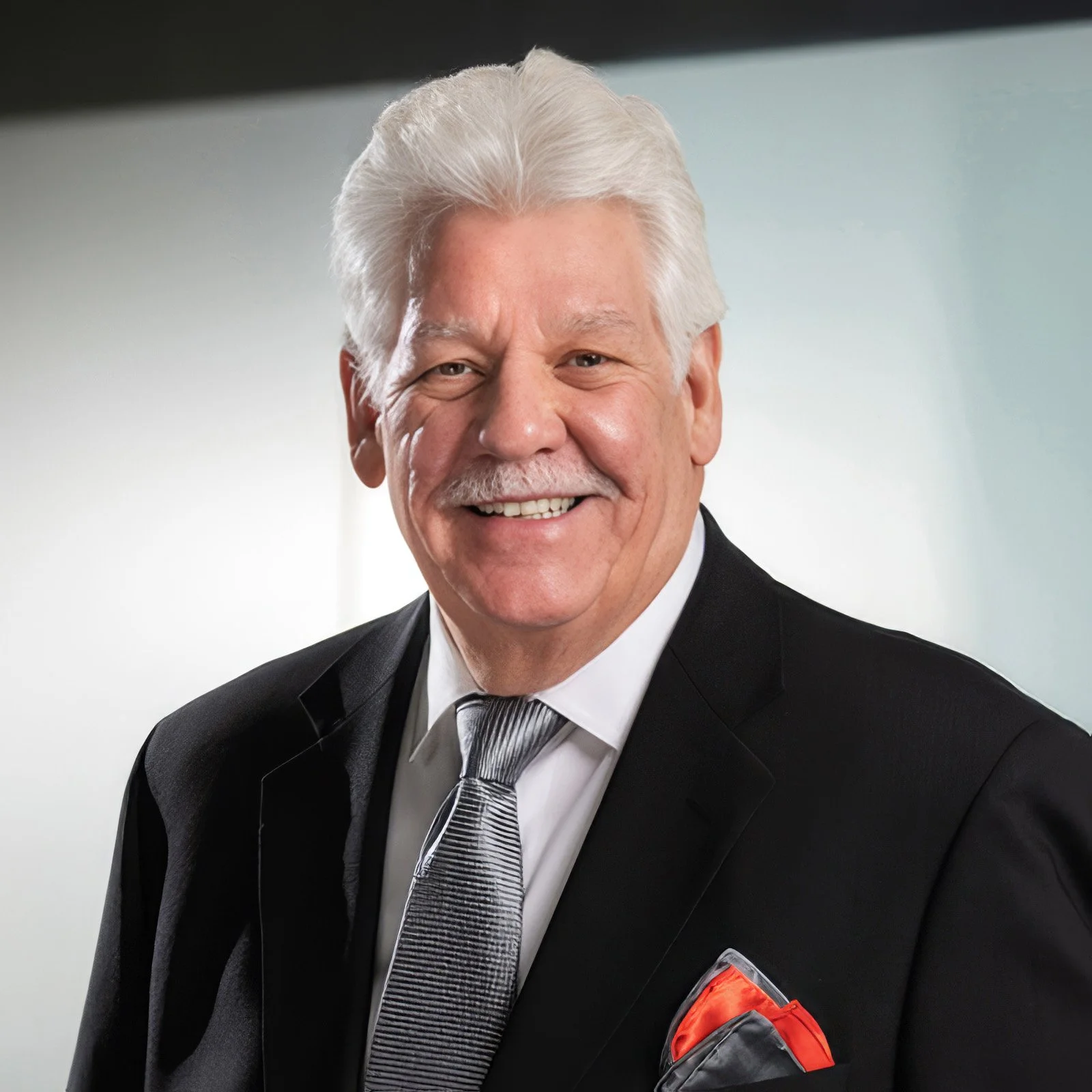 Smiling older man in a business suit against a blue gradient background.