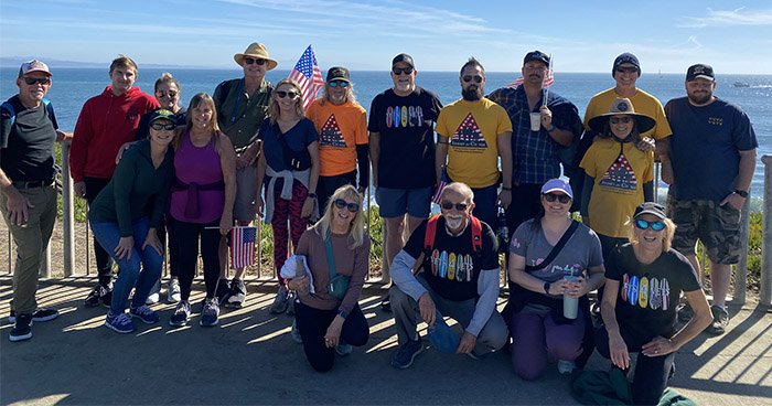 Group posed in front of an ocean view for the 2023 veterans day walk, with some people carrying flags.