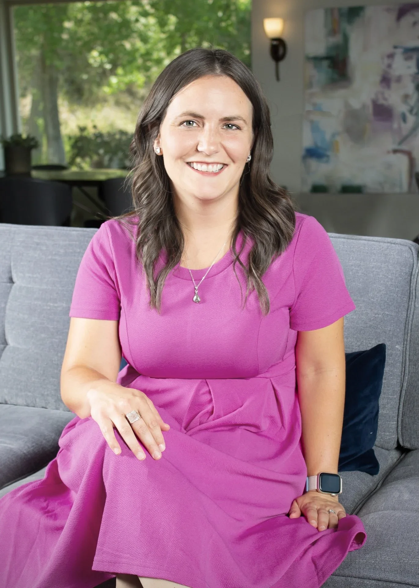 Smiling woman with long wavy hair wearing a white sleeveless top, photographed against a white background.