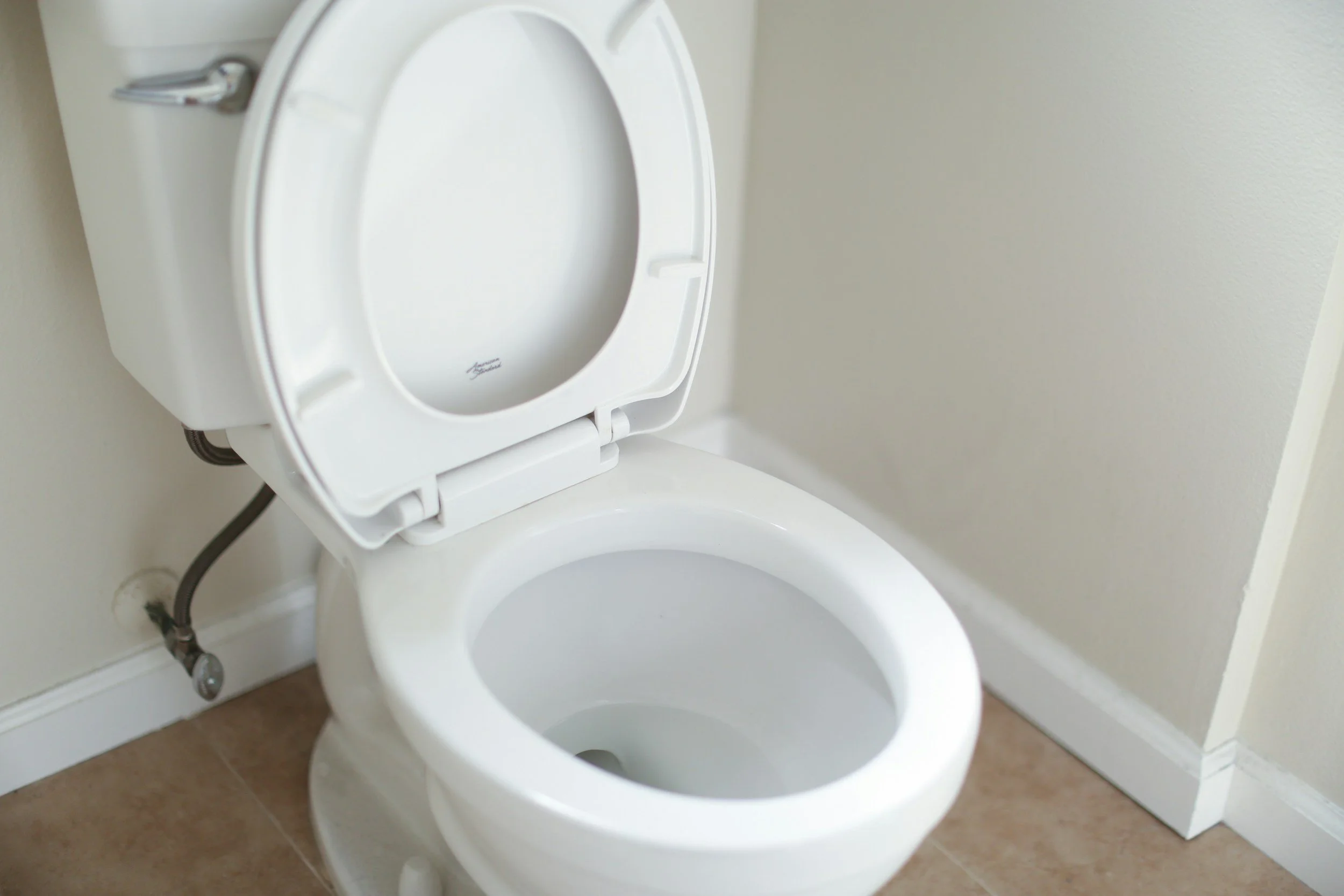A white toilet with the lid upright in a bathroom with beige walls and tiled floor.