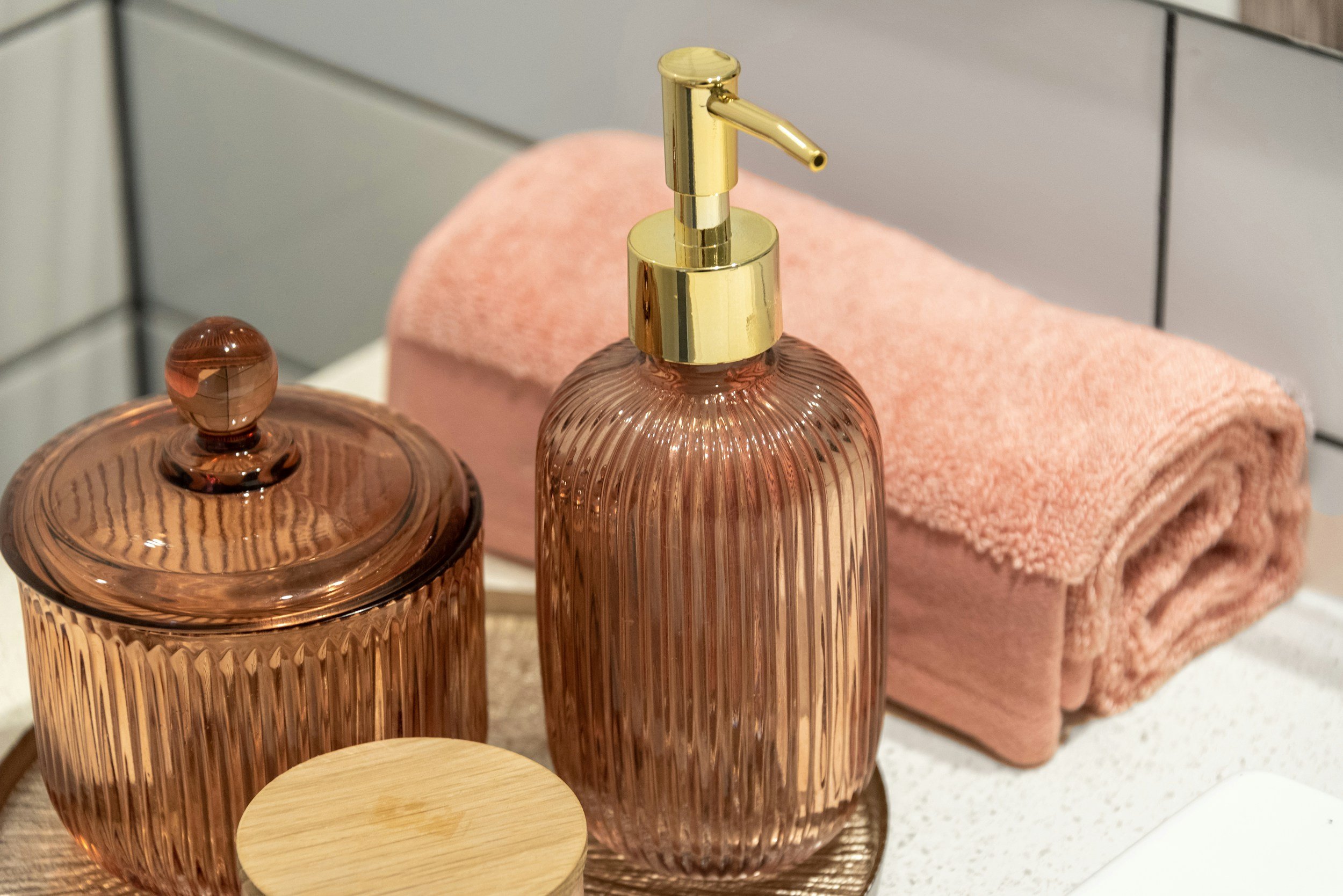 Pink rolled towel, pink soap dispenser with gold pump, pink jar with lid, and pink container on a bathroom counter.