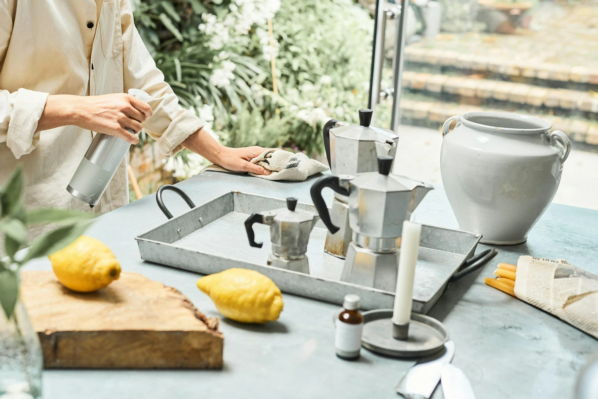Person wiping a kitchen counter with lemons, candlestick, and coffee moka pots on the table.